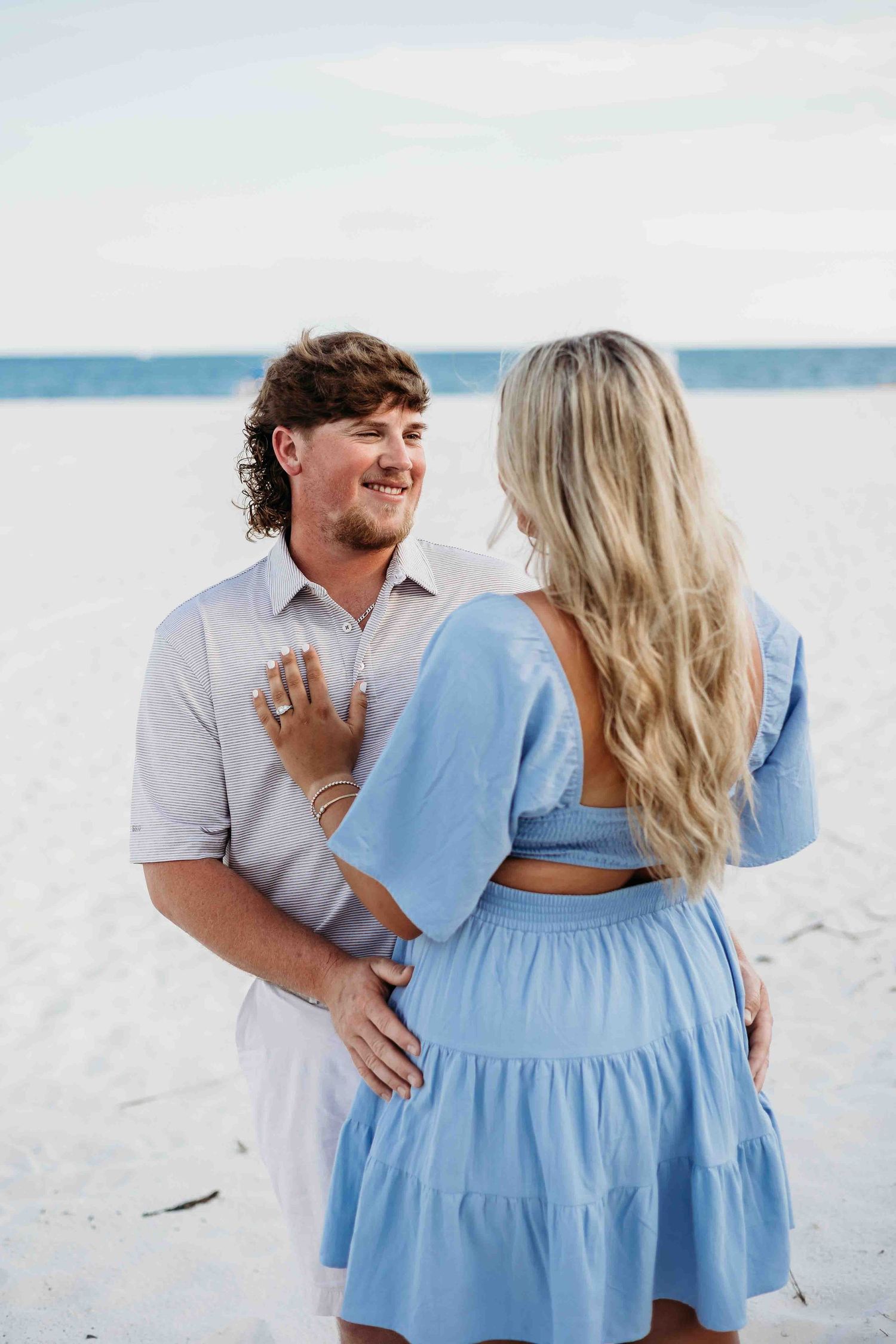 Couple in light blue dress and white shirt sharing joyful moment on beach.