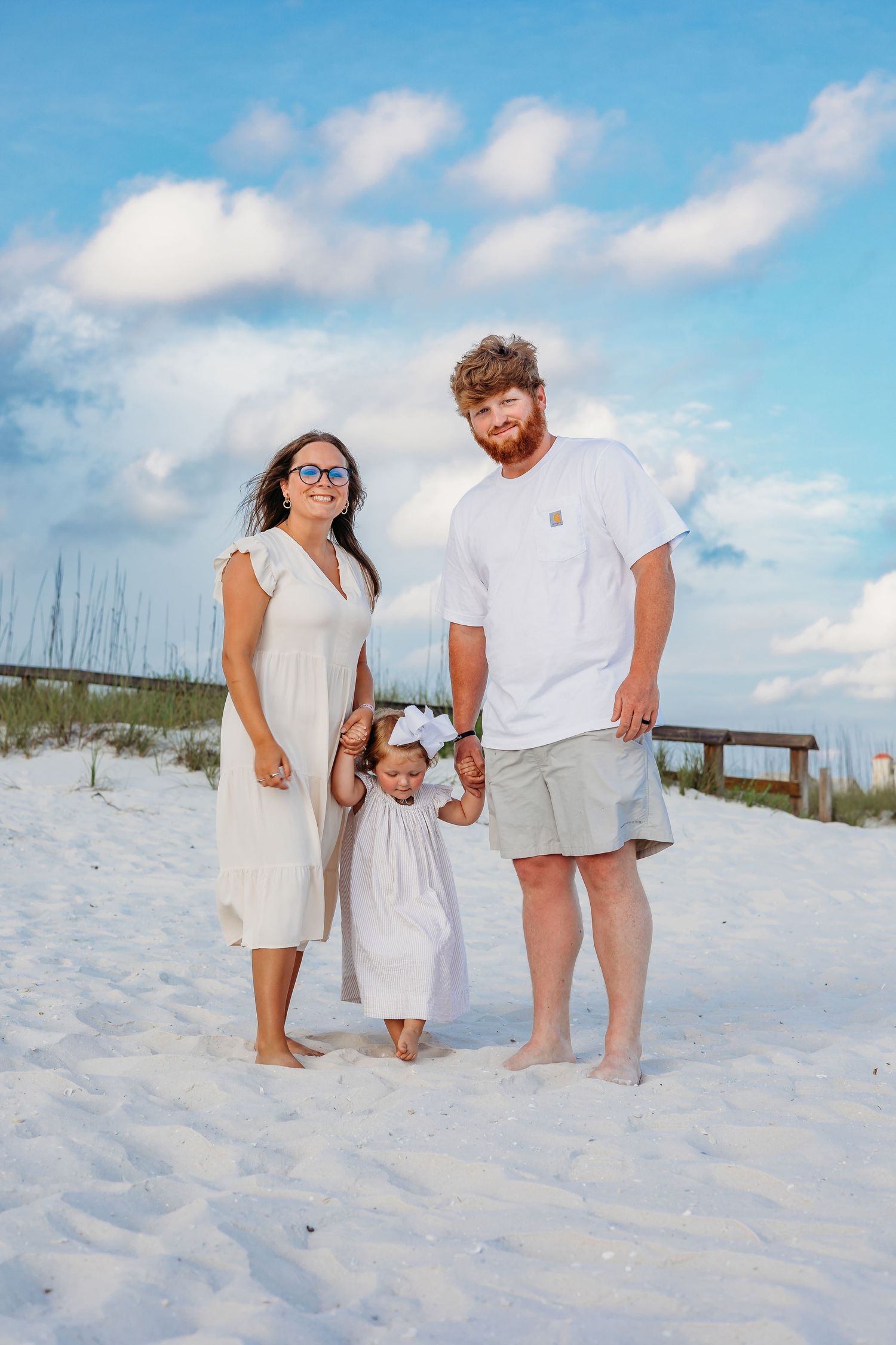 A family wearing white outfits poses together on a pristine white sand beach under blue skies.