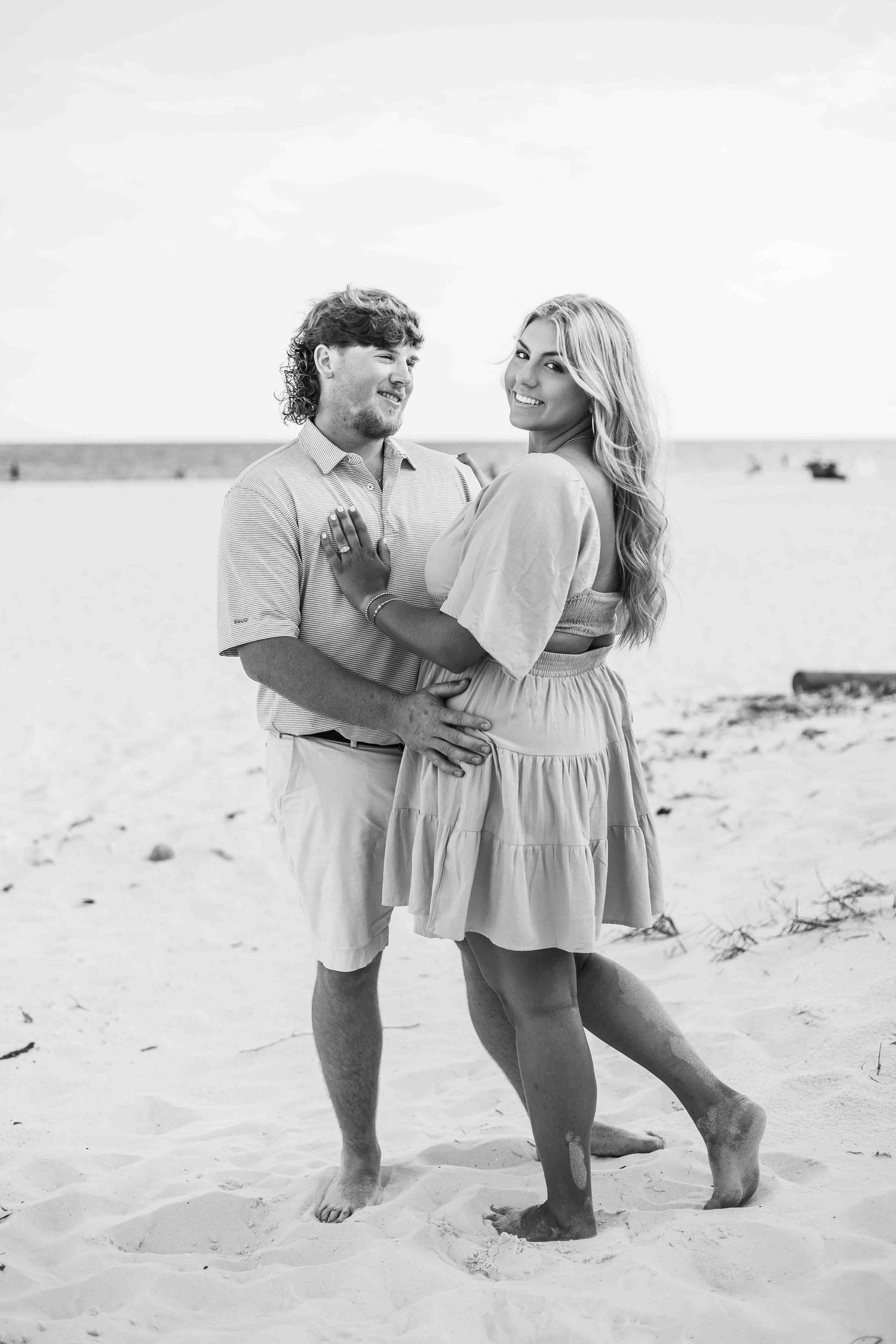Black and white photo of couple dancing barefoot in sand during beach engagement.