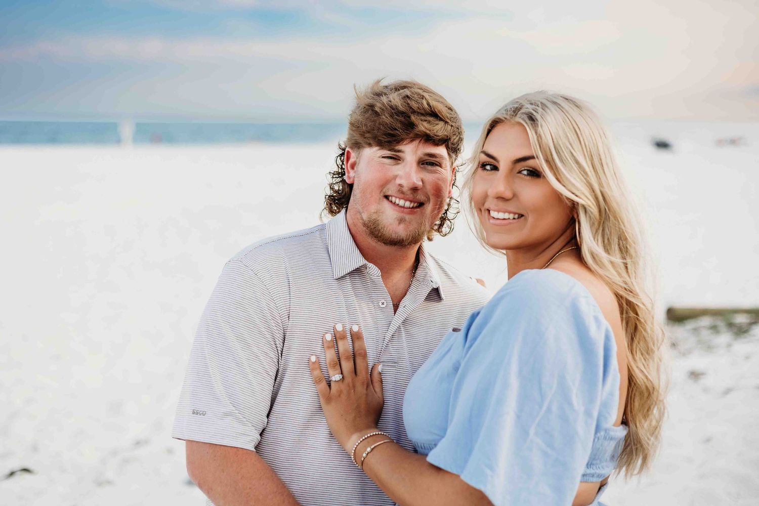 Romantic beach engagement photos with couple in coordinated blue and white outfits.