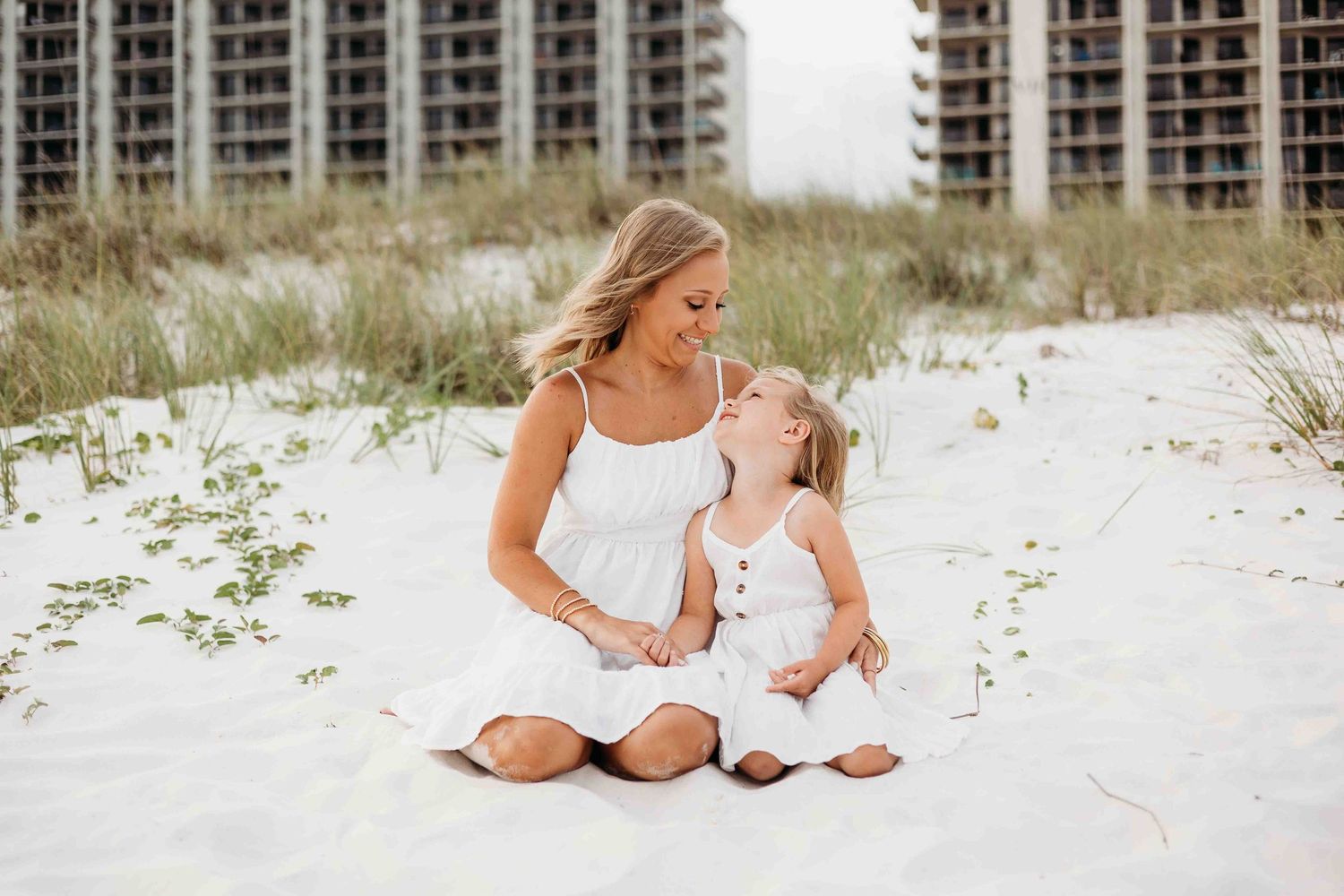 Family portrait session on white sand beach with high-rise buildings in background.