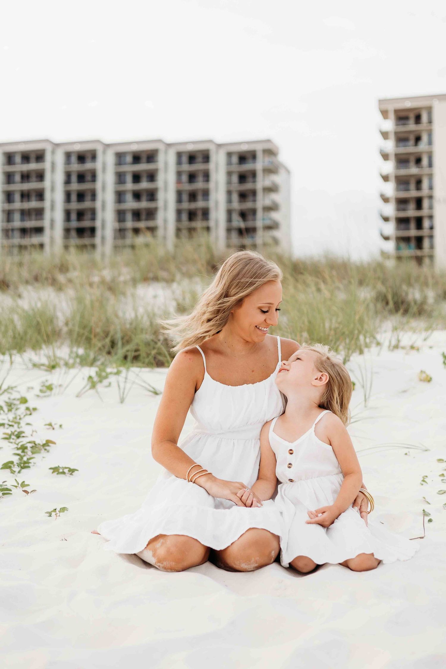 Beachside family photography session with coastal buildings visible in background.