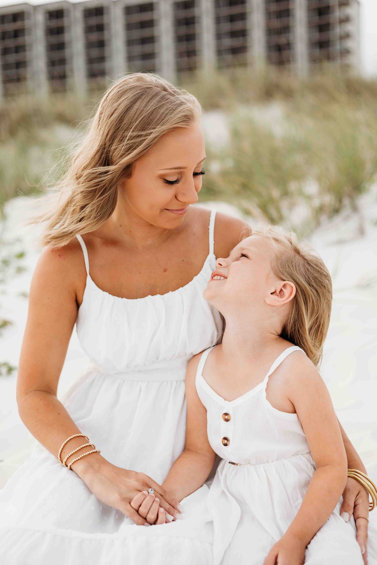 Sweet candid moments between parent and child wearing white dresses on the beach.