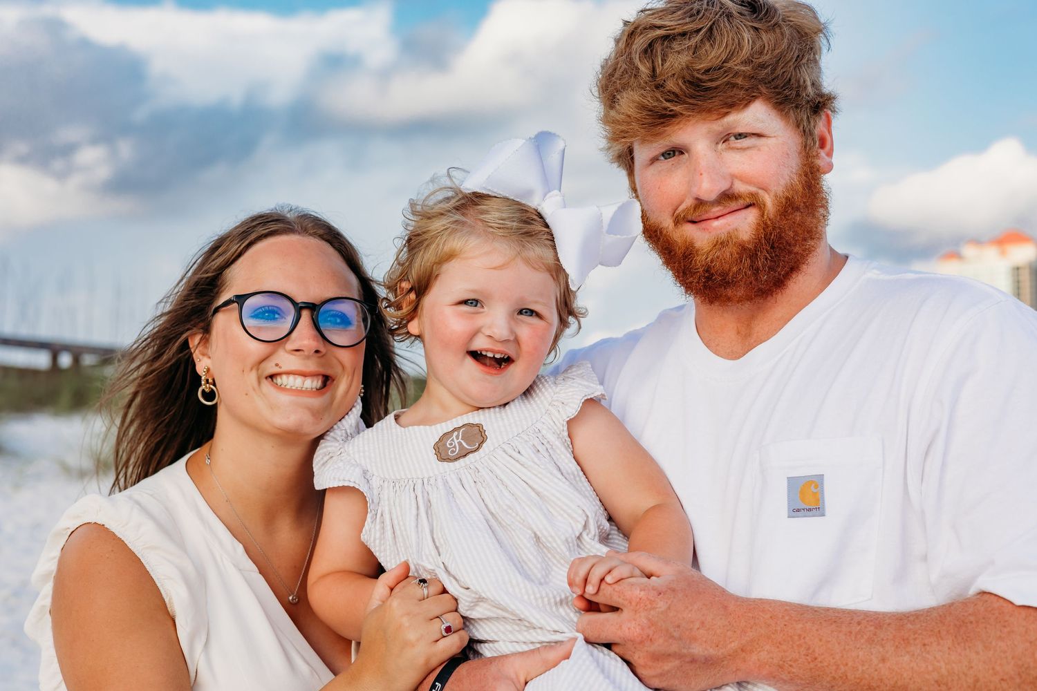 Close-up beach portrait of a family group smiling together against a bright blue sky.