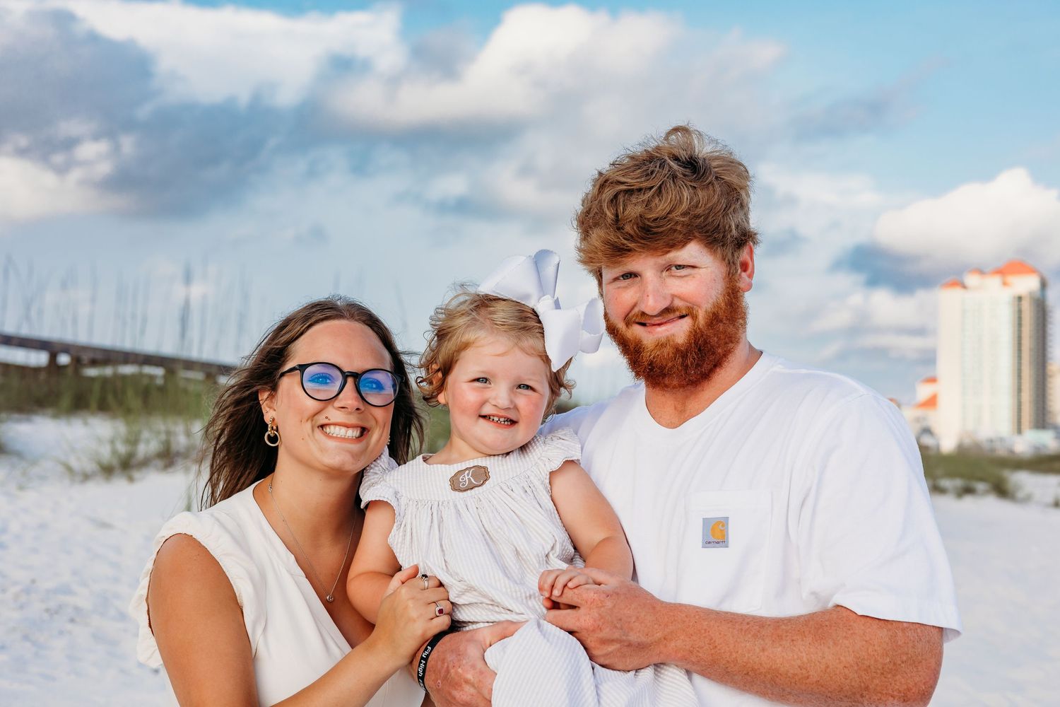 A family shares a joyful moment together on a white sandy beach with coastal buildings in the background.