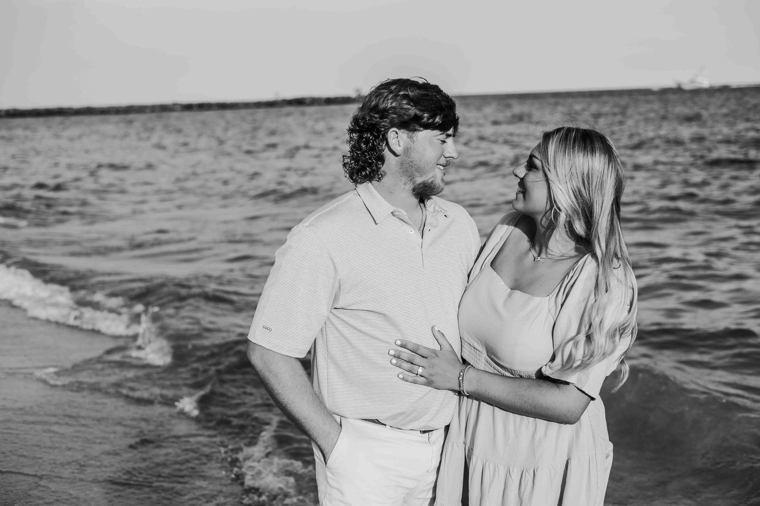 Black and white photo of a couple sharing an intimate moment on the beach at sunset.