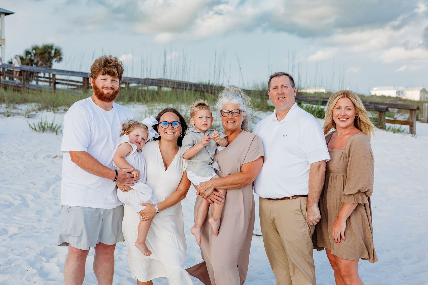 A multi-generational family poses together on a white sandy beach during a sunny day.