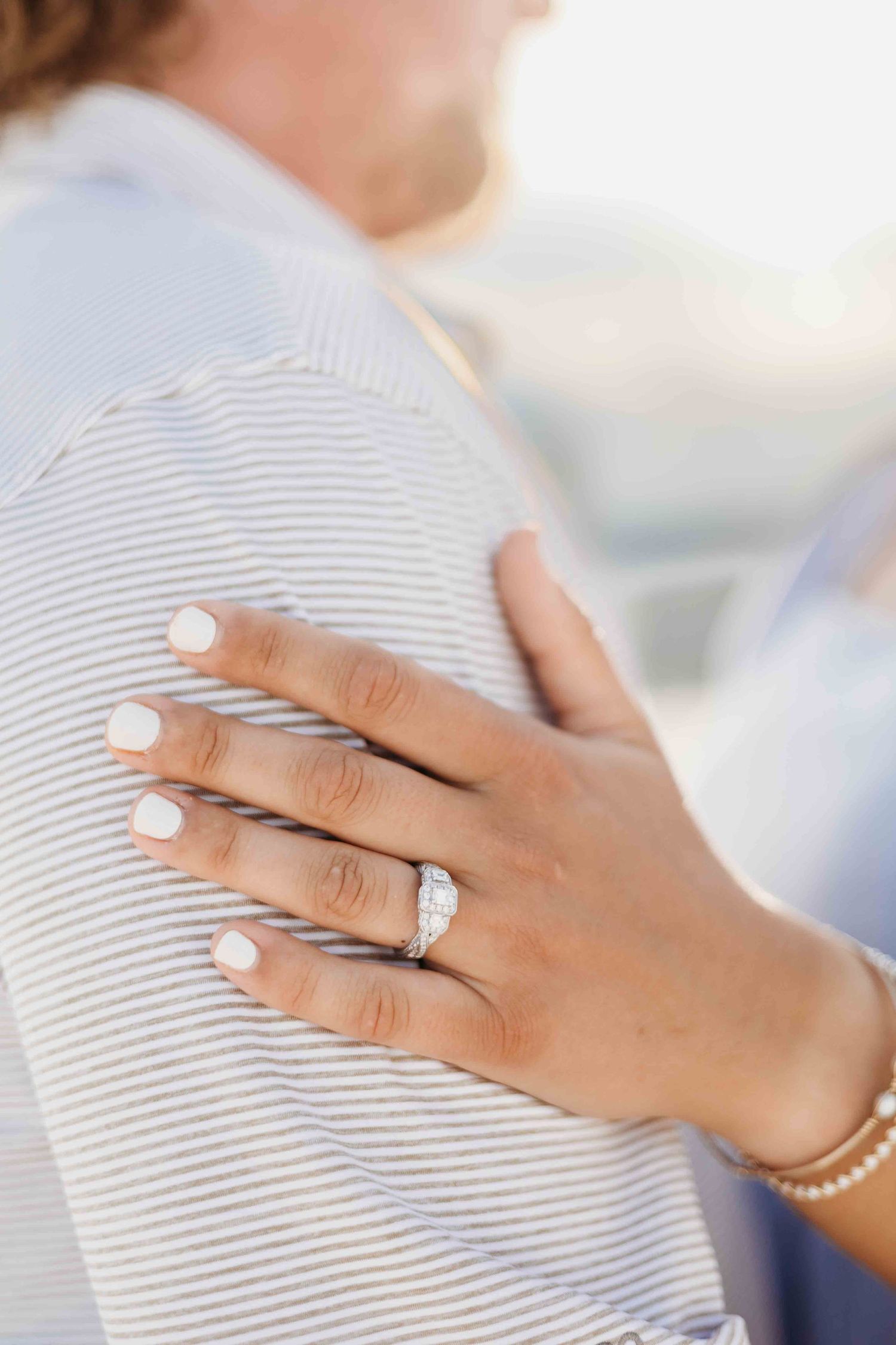 Close-up of a hand wearing an engagement ring against a striped fabric background.