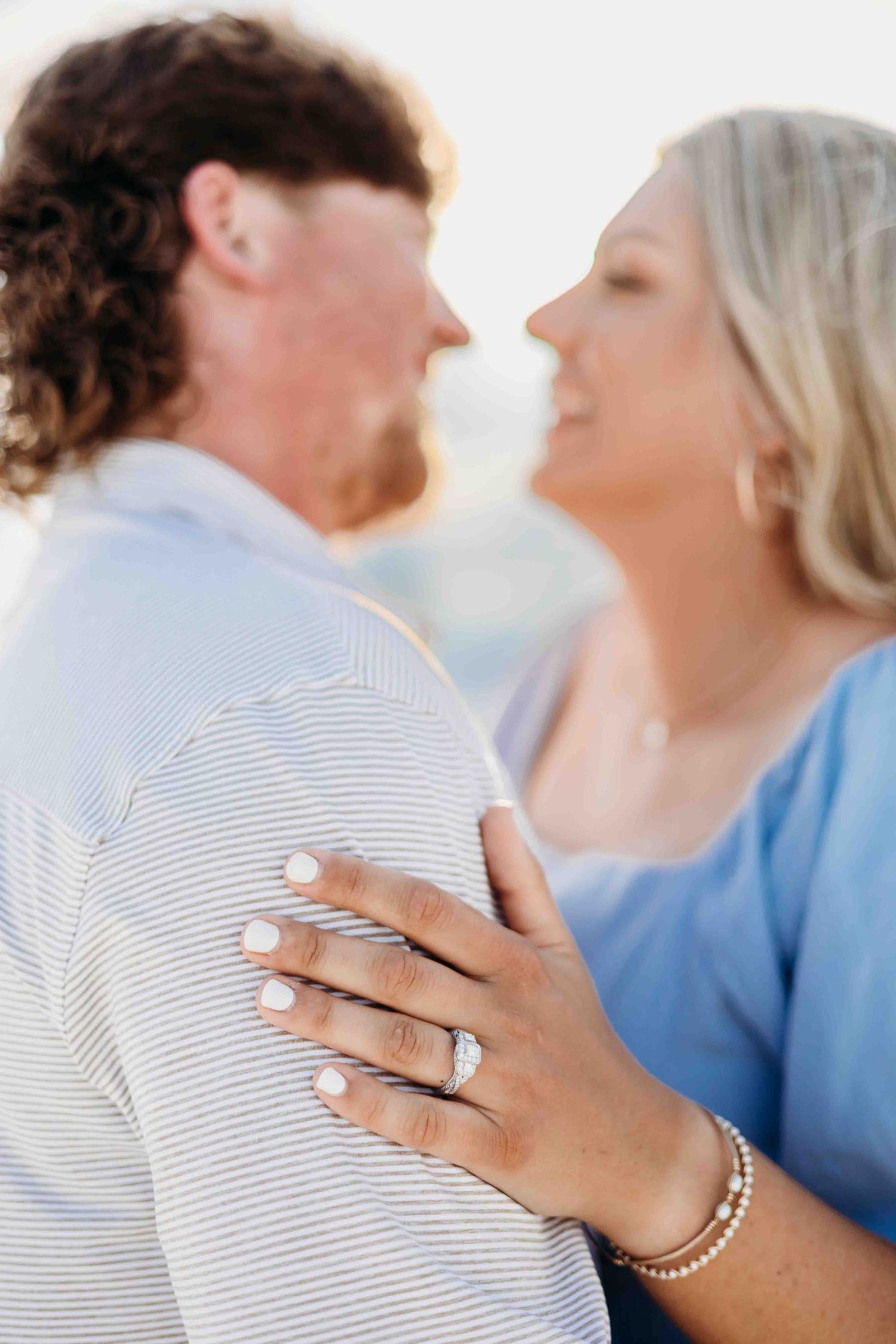 Close-up profile view of a couple with hand displaying engagement ring against striped shirt.