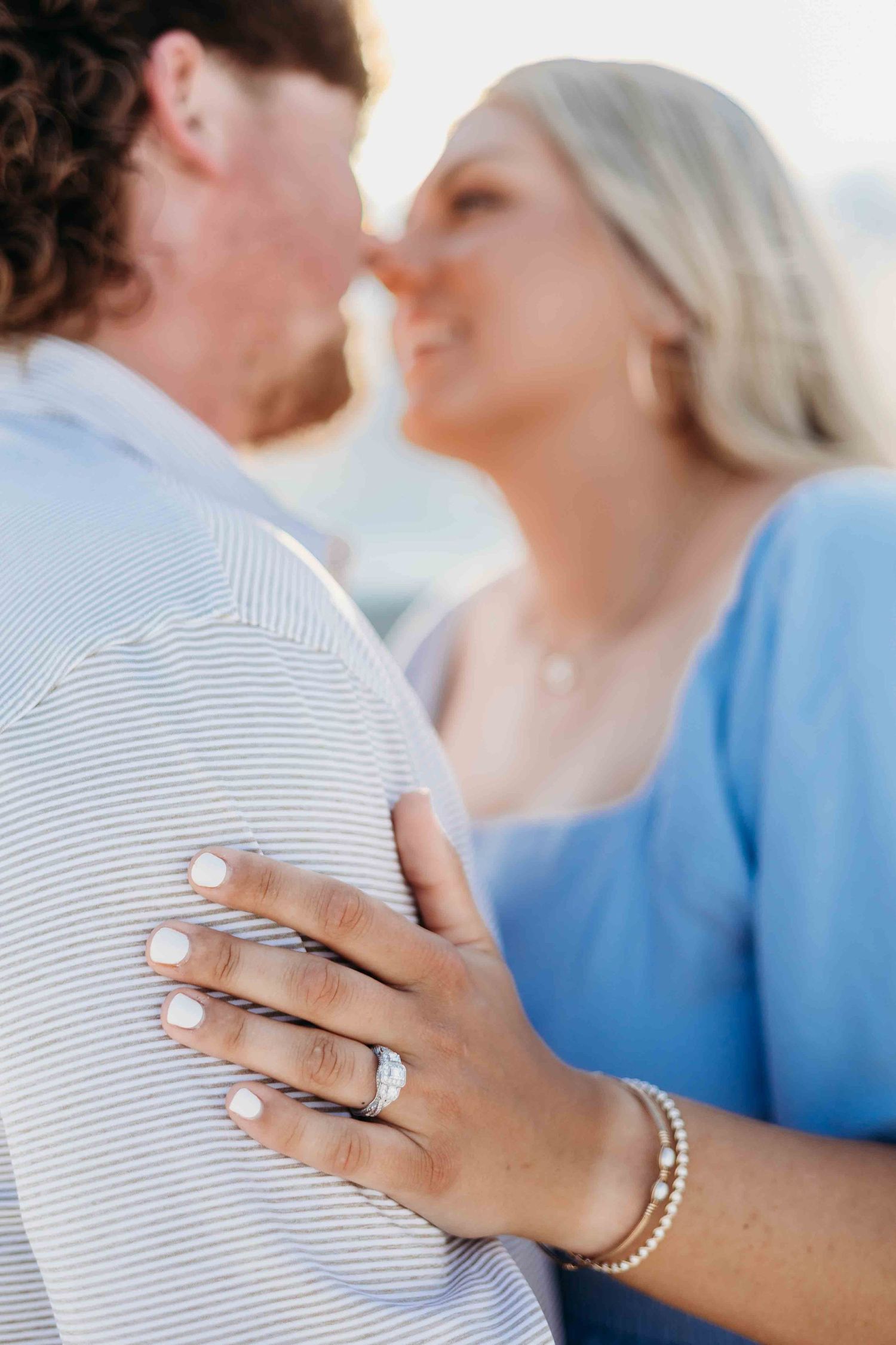 Romantic engagement photo showing ring detail while couple embraces on beach.