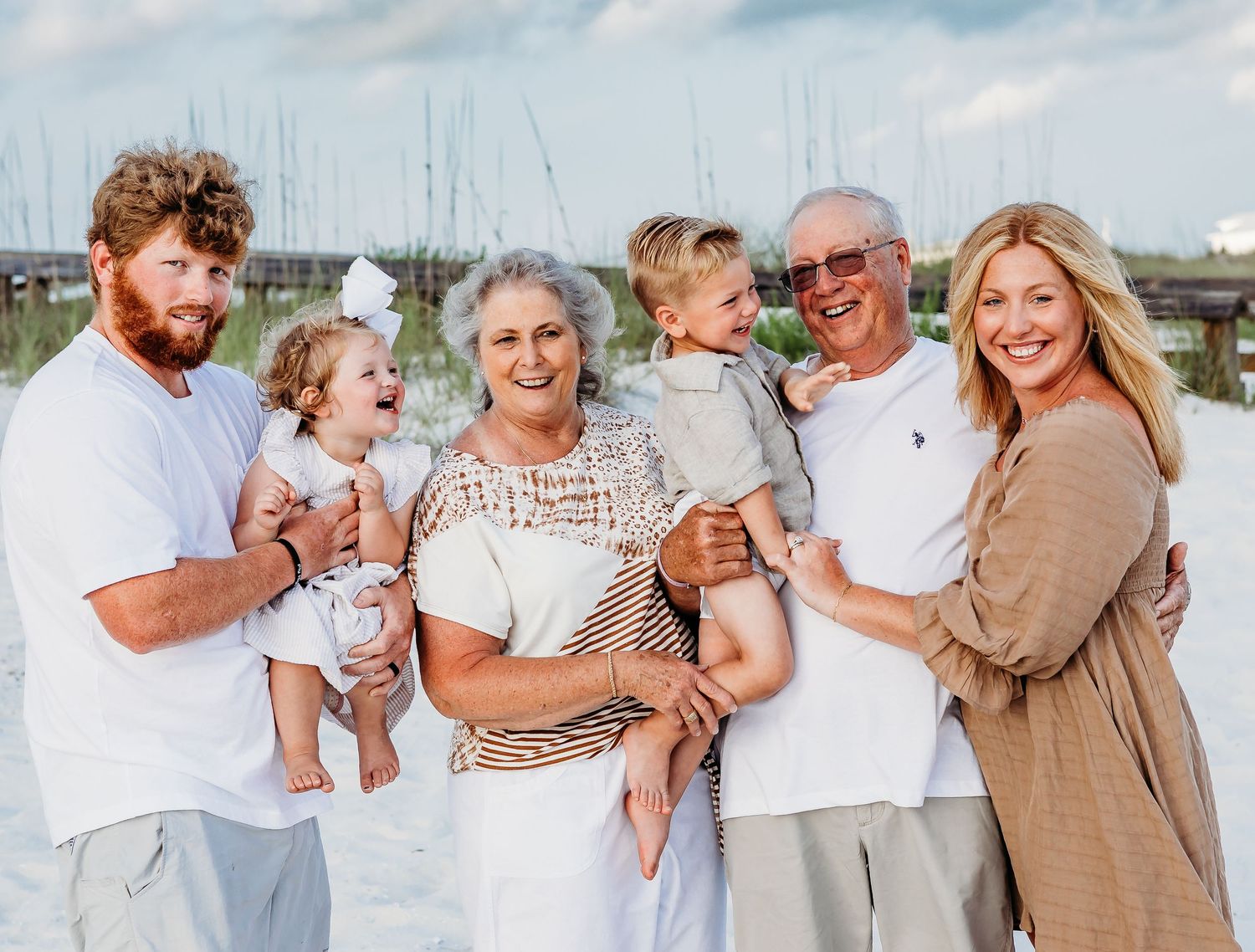 Family group photo on a beach with coastal architecture visible in the background.