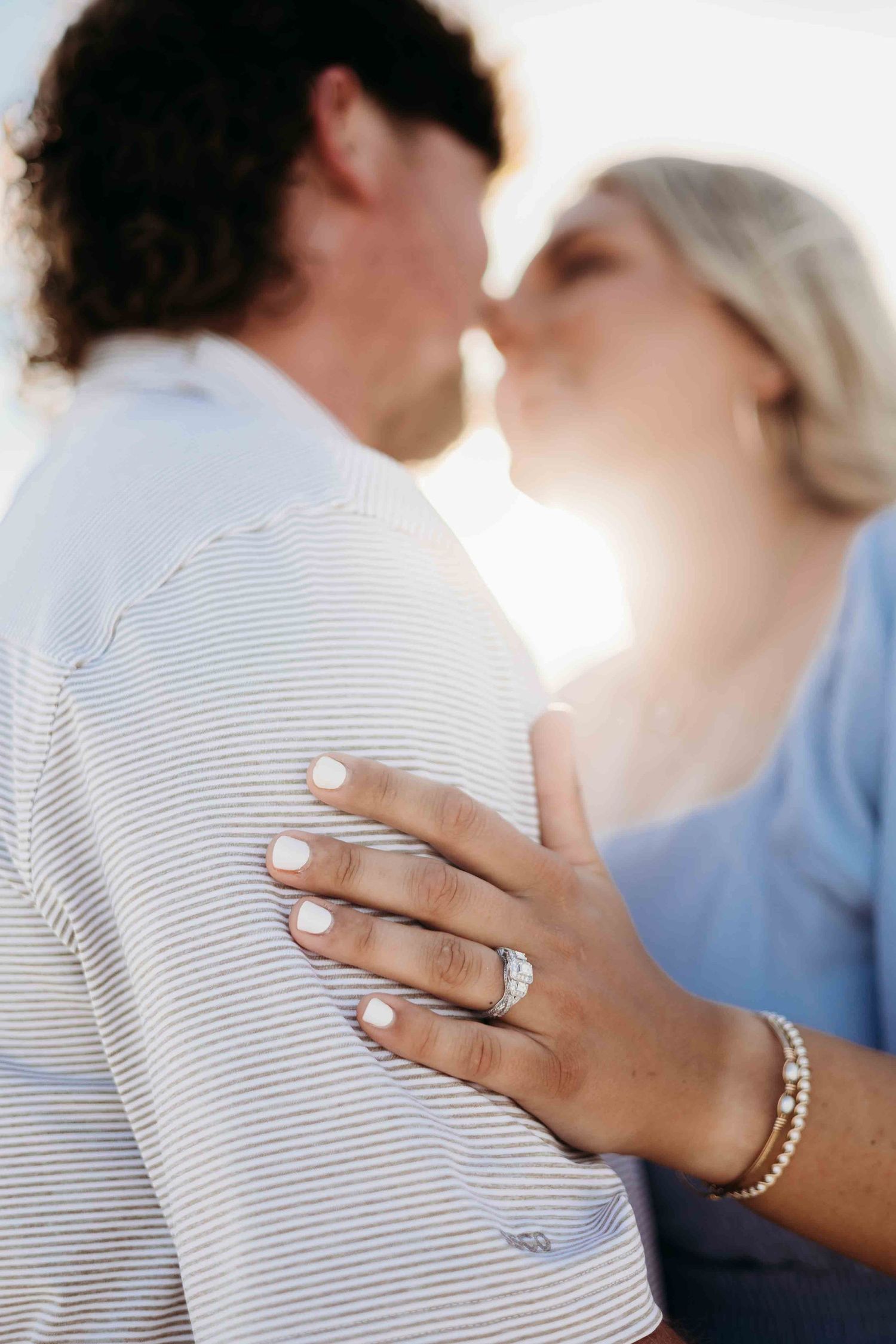 Sunlit engagement photo capturing ring detail and intimate moment between couple on beach.