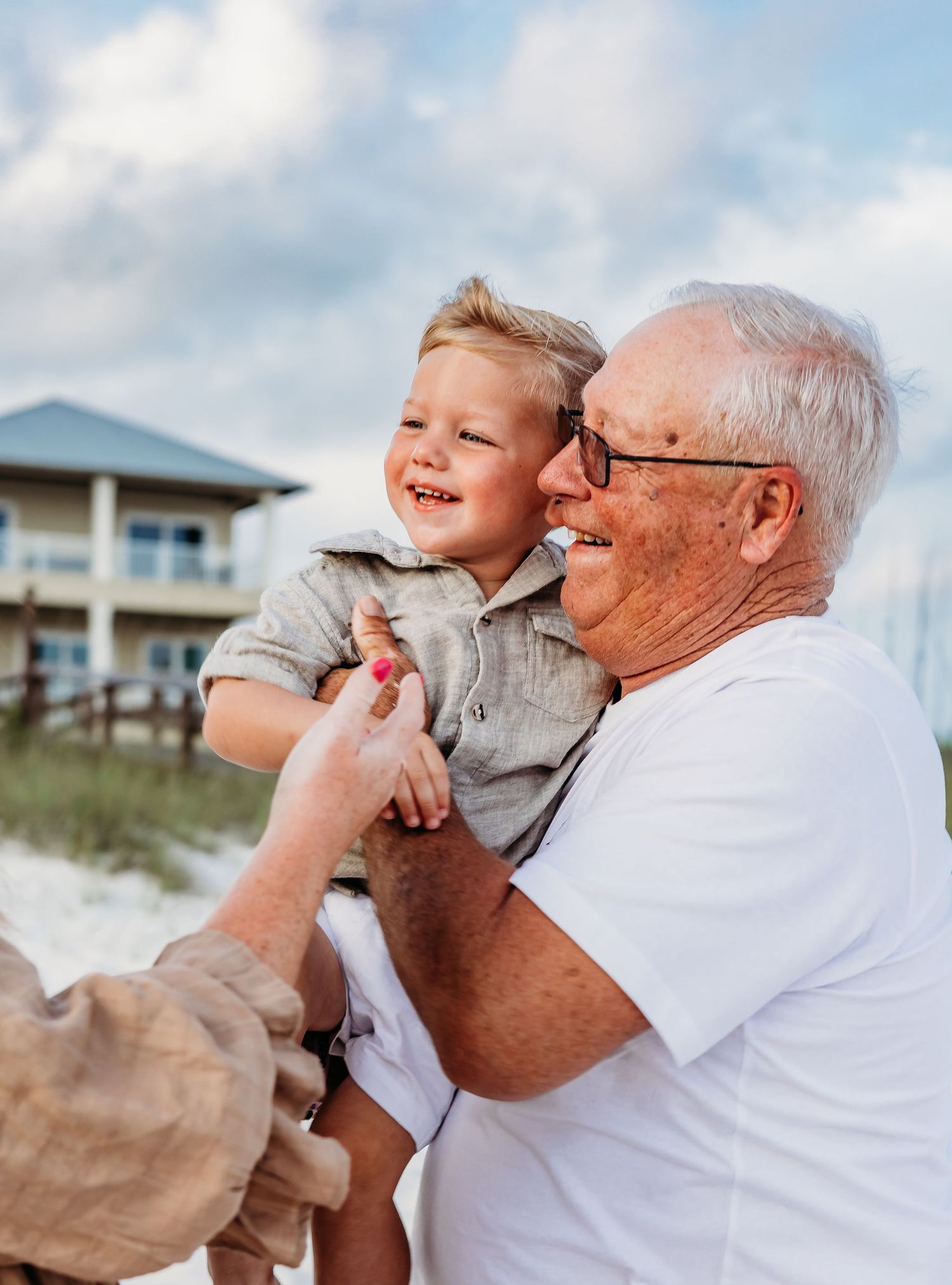 Playful beach moments between family members with coastal homes in background.
