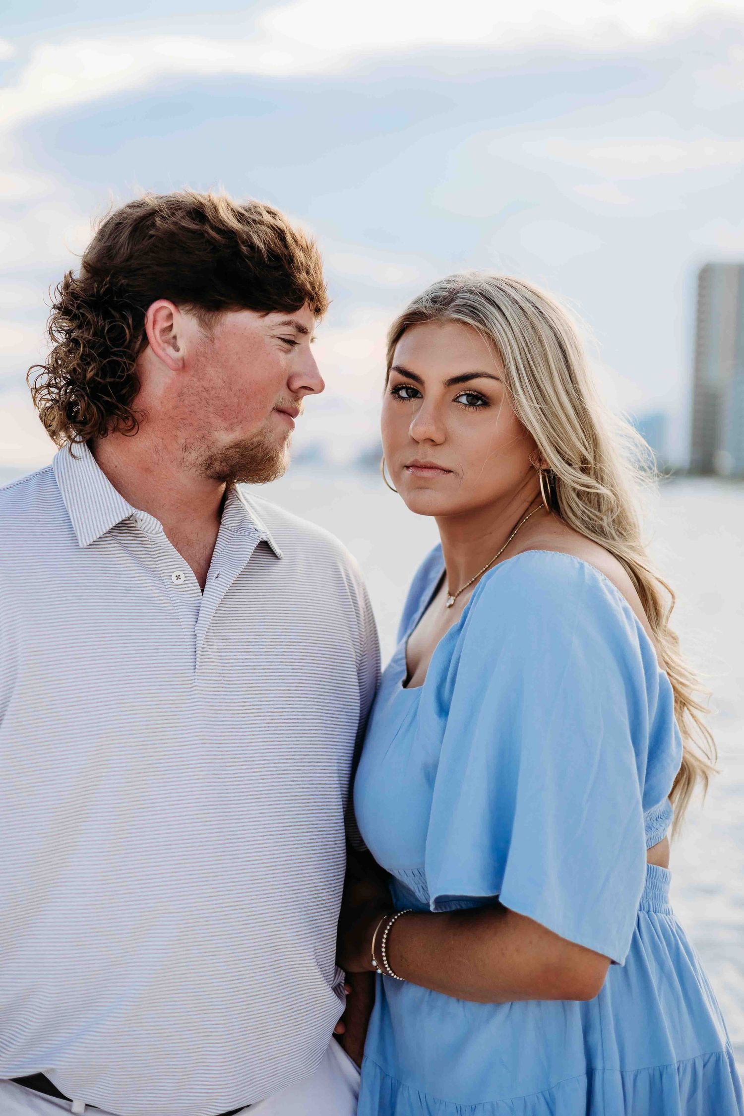 Romantic couple in coordinated outfits pose together against a coastal backdrop.