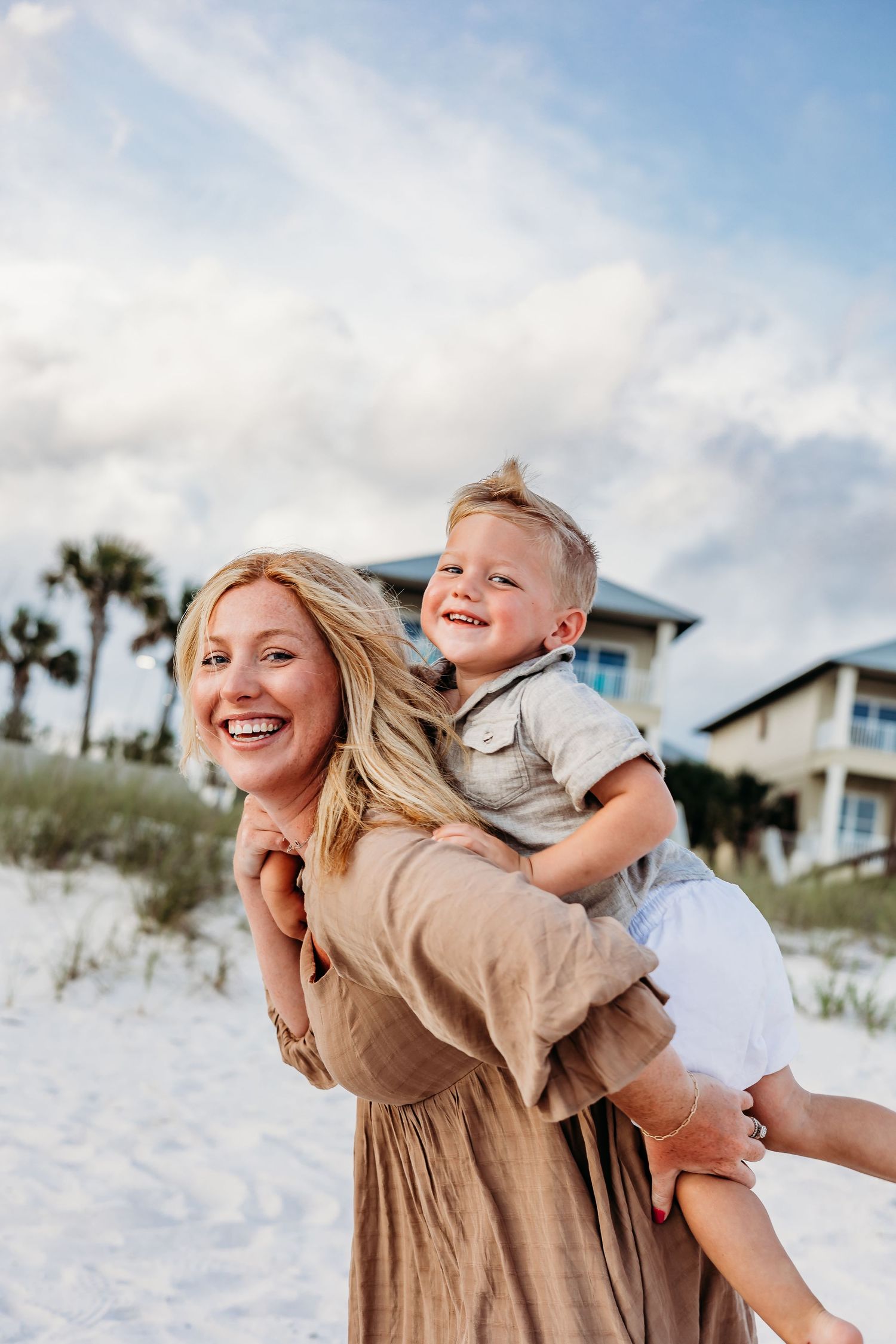 Mother and child playing together on a white sandy beach with palm trees and blue skies.
