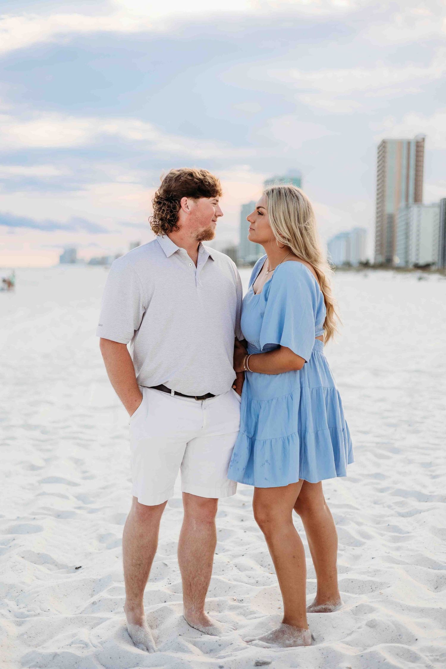 Couple walking together on white sand beach wearing matching light colored outfits.