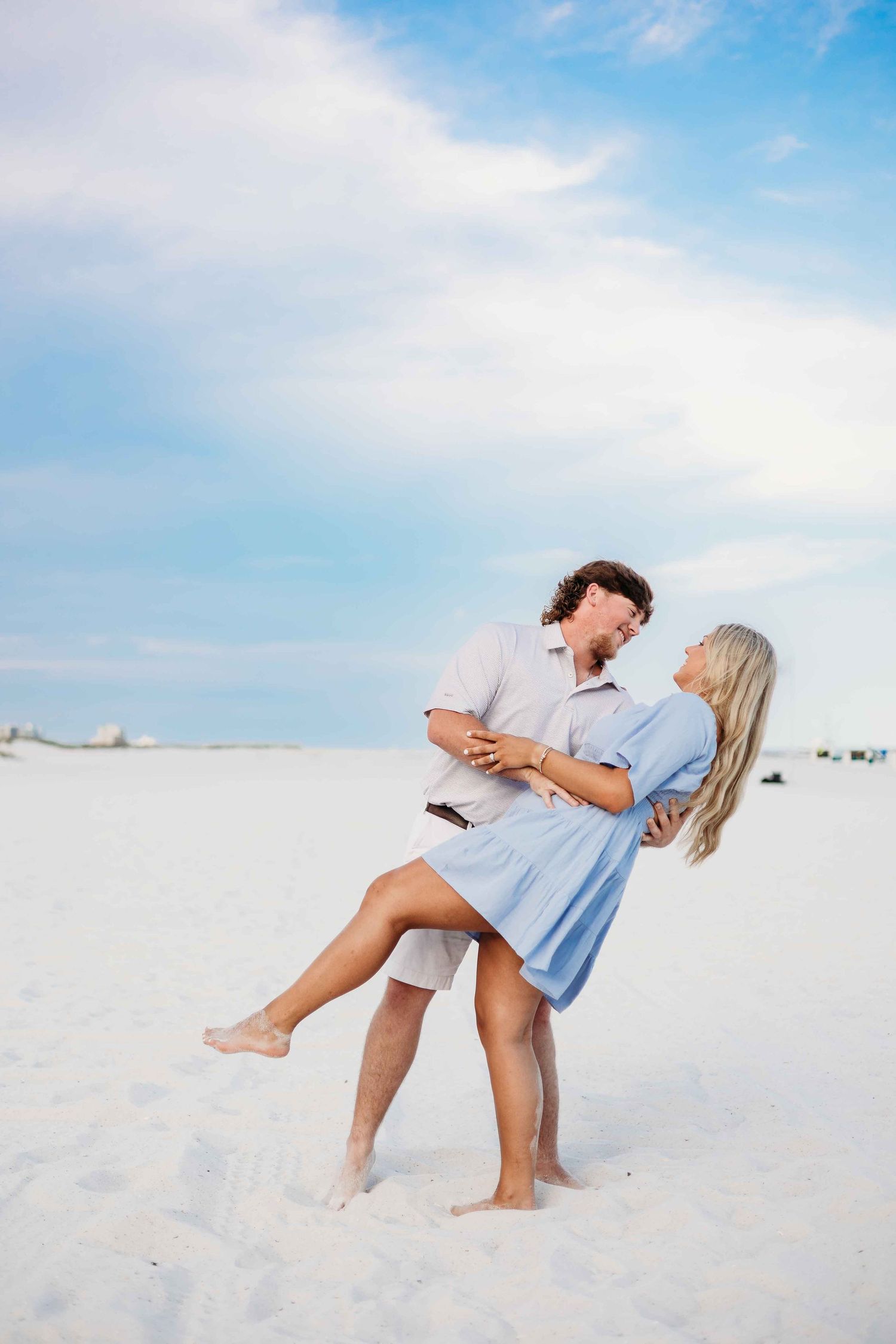 Playful couple poses on white sand beach during sunset photoshoot.