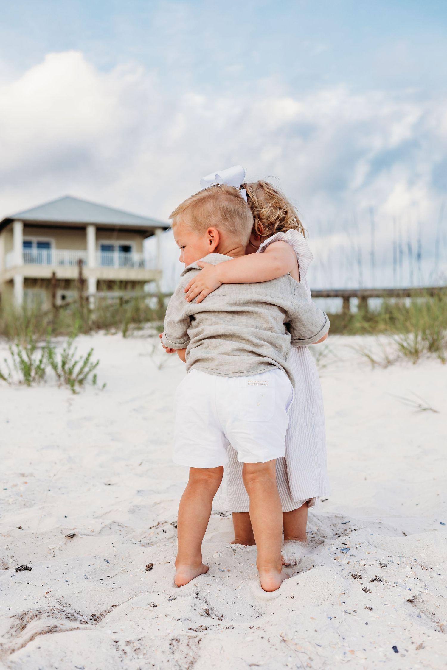 Tender family moments captured on white sandy dunes with beach houses in background.