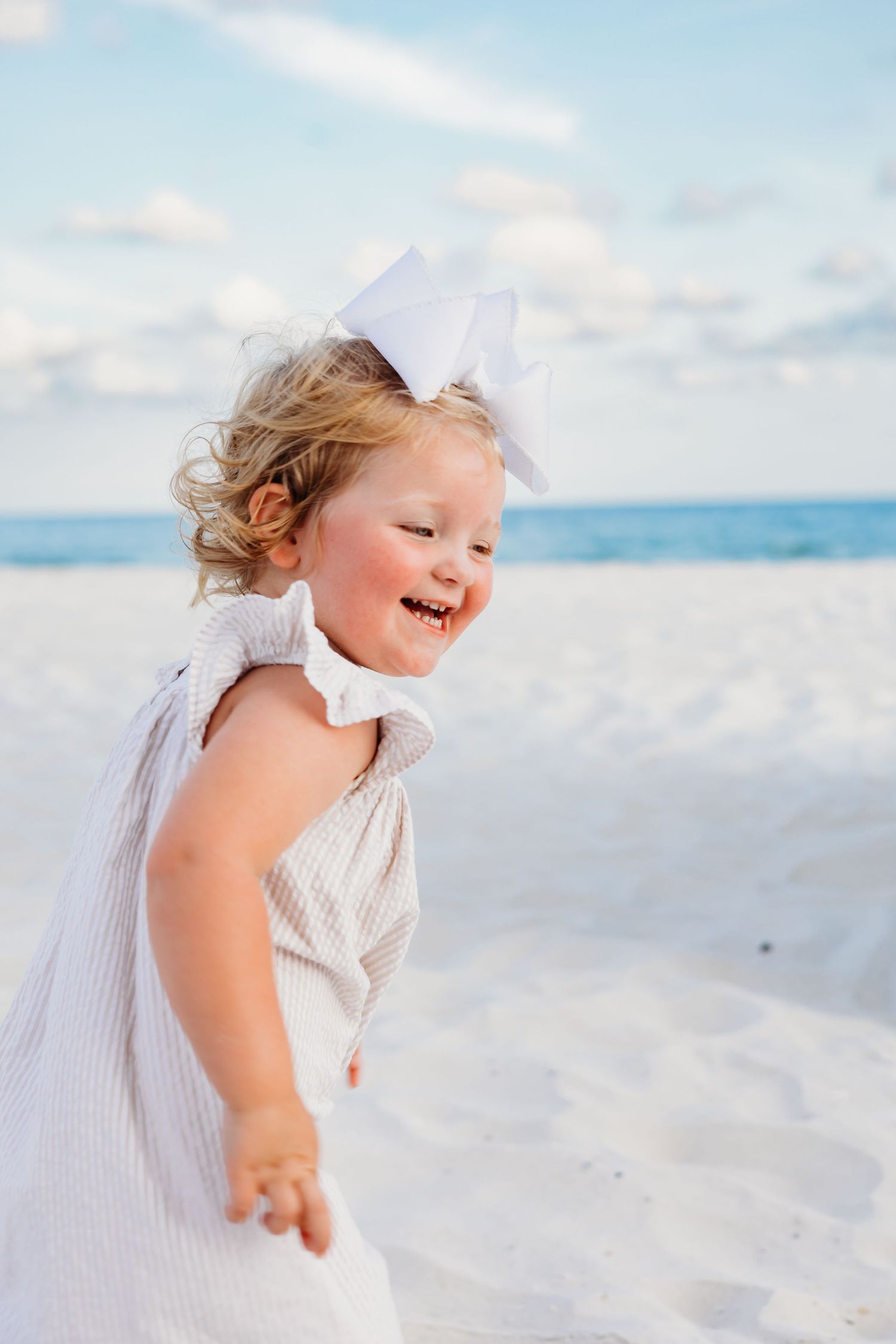 Joyful young child laughing while playing on pristine white beach sand.