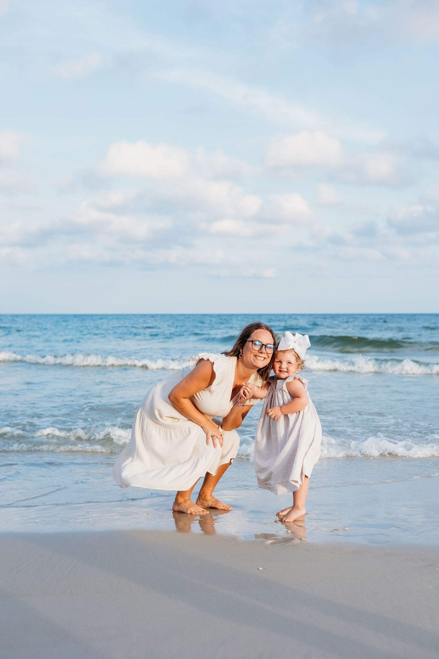 Two people in white dresses playing together at the edge of the ocean waves.