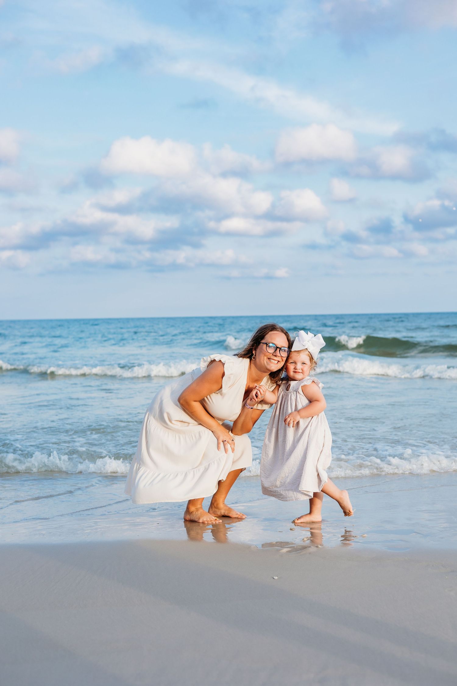 Two figures in white outfits share a playful moment along the shoreline.