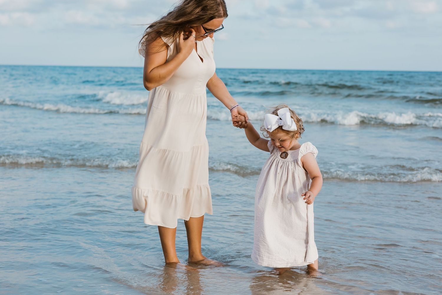 People in flowing white dresses walking along the beach at sunset.