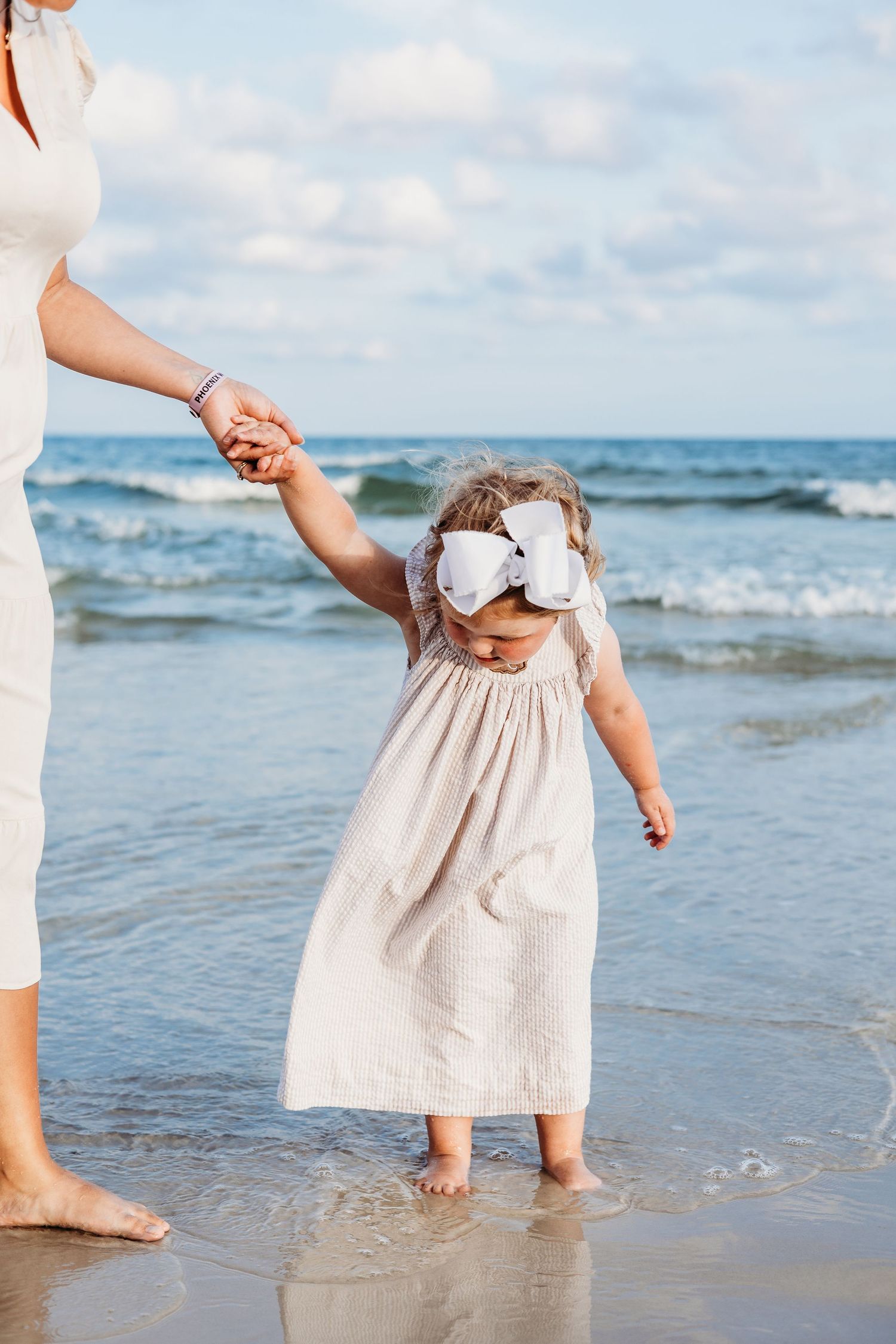 Close-up of bare feet and white dress hems walking in shallow ocean water.