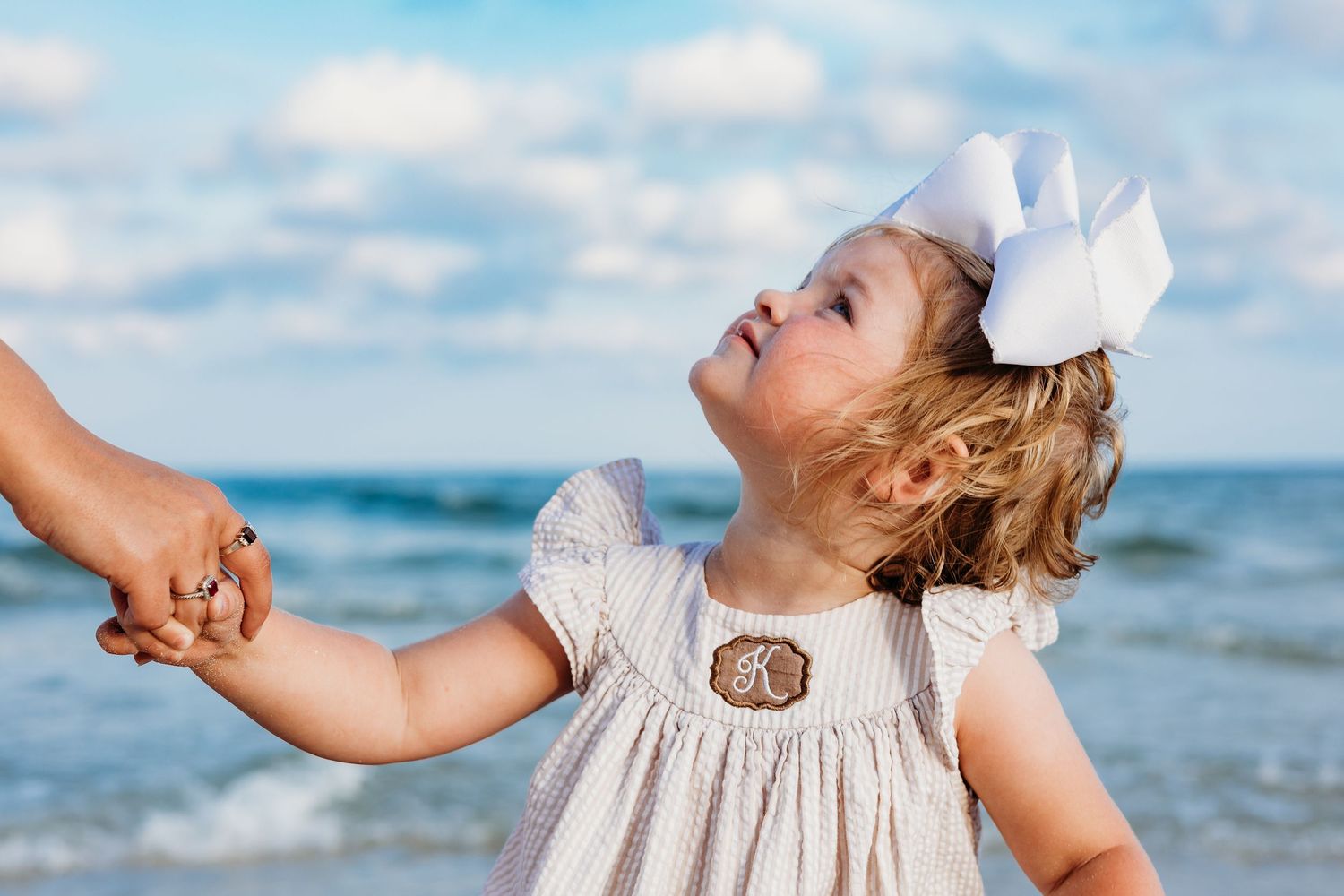 Small child in a white dress and bow playing at the beach.