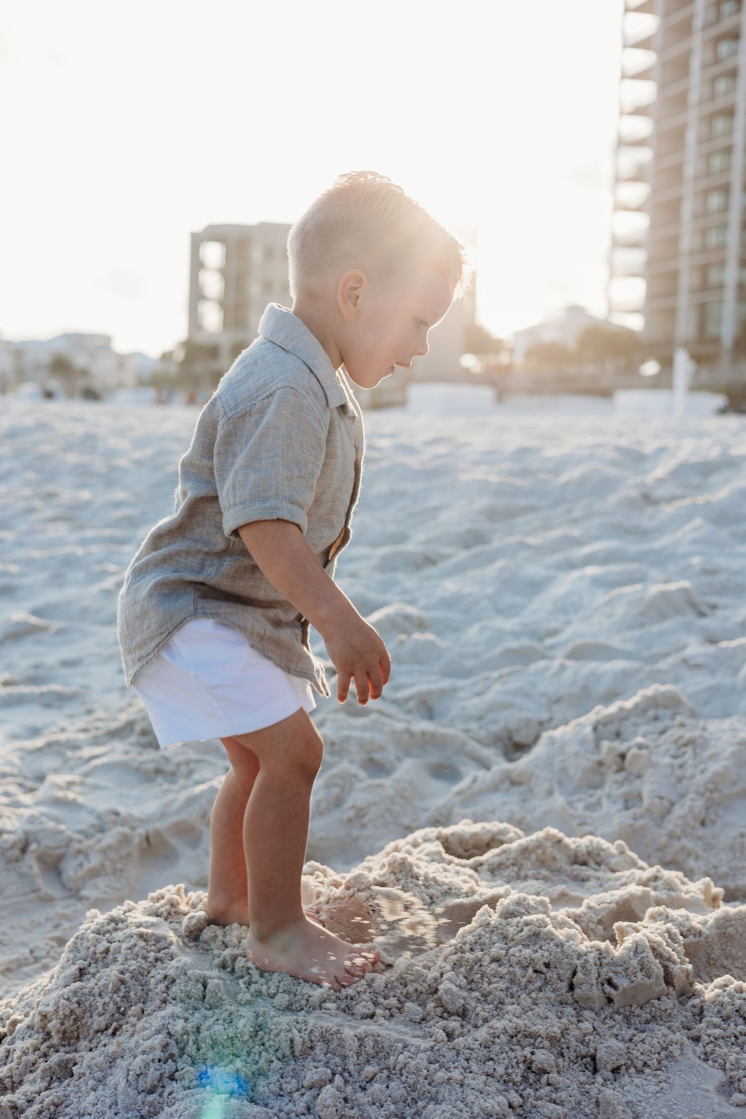 Small child playing in beach sand during golden hour with buildings in background.