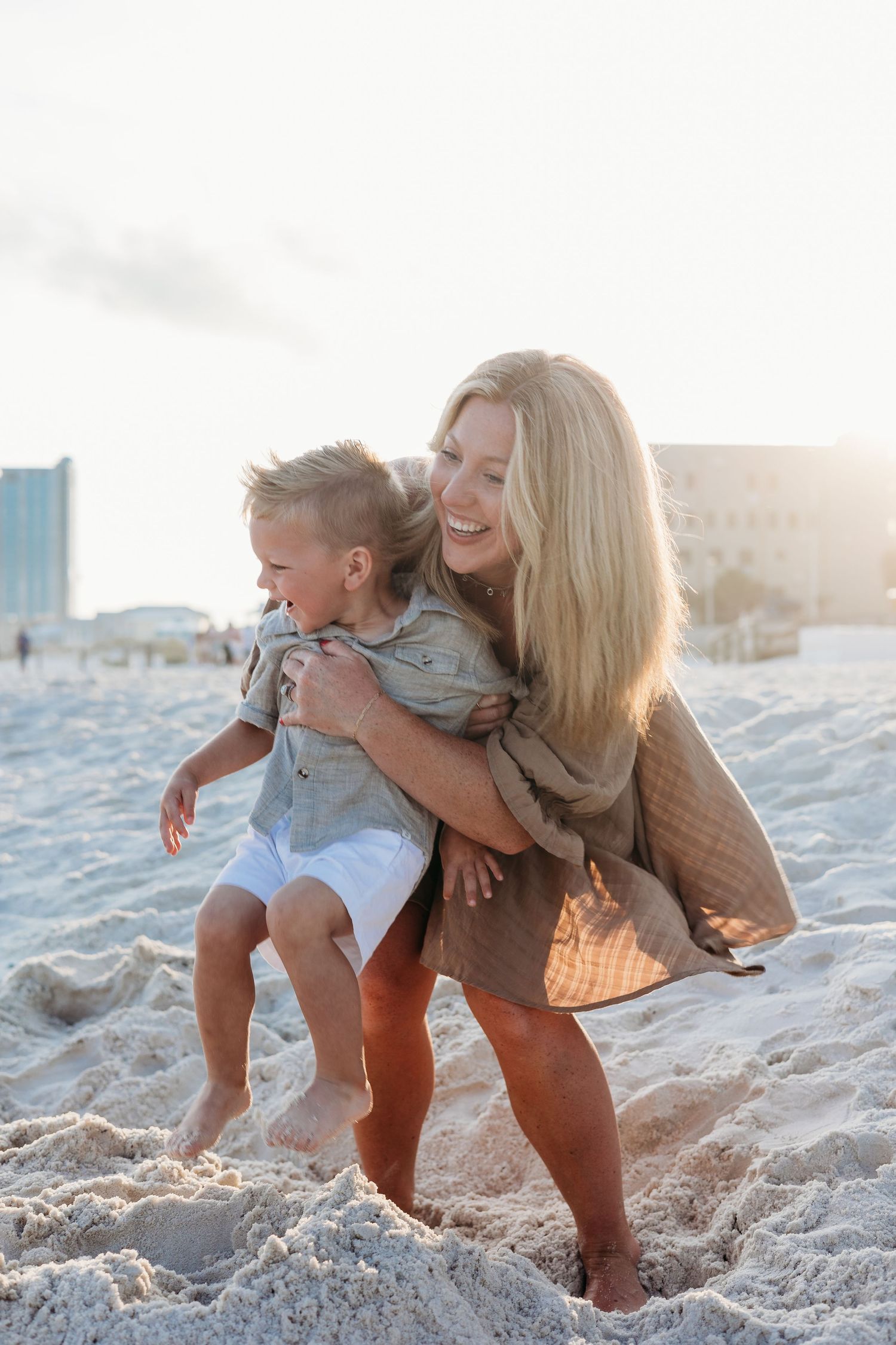 A playful moment captured on the beach with joyful embraces and laughter in the sand at sunset.