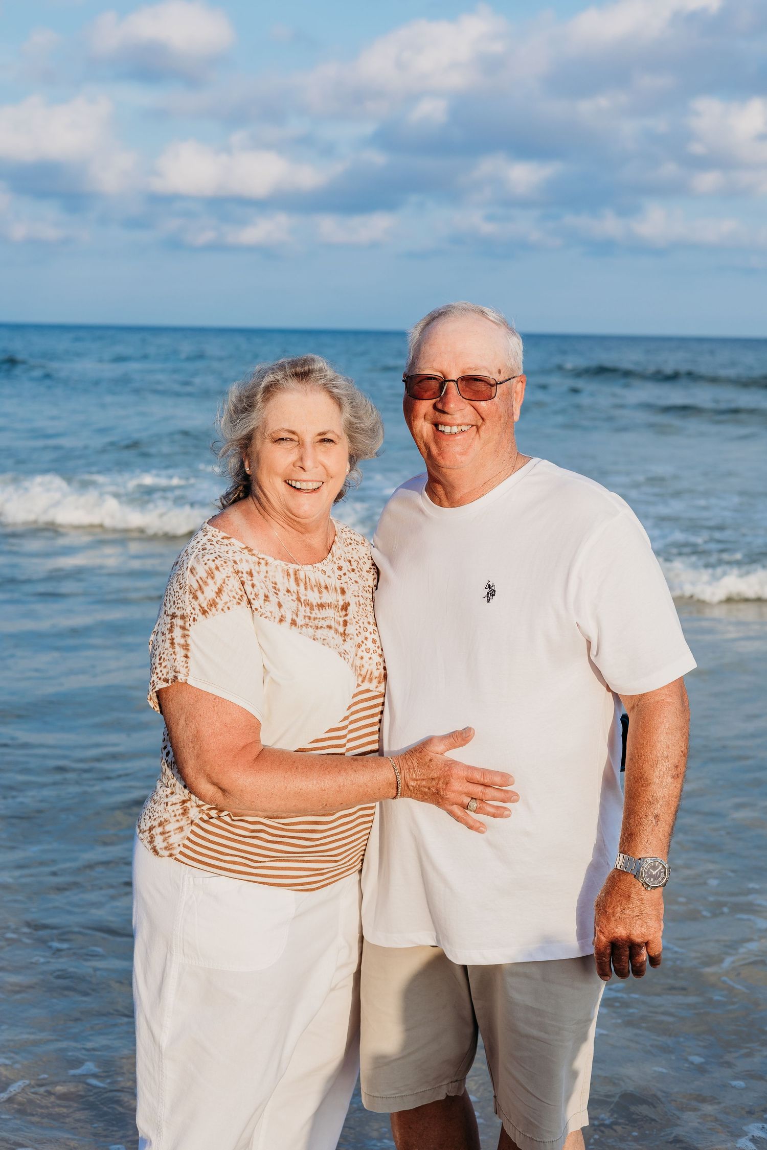 Senior couple sharing a tender moment on the beach with ocean waves in the background.