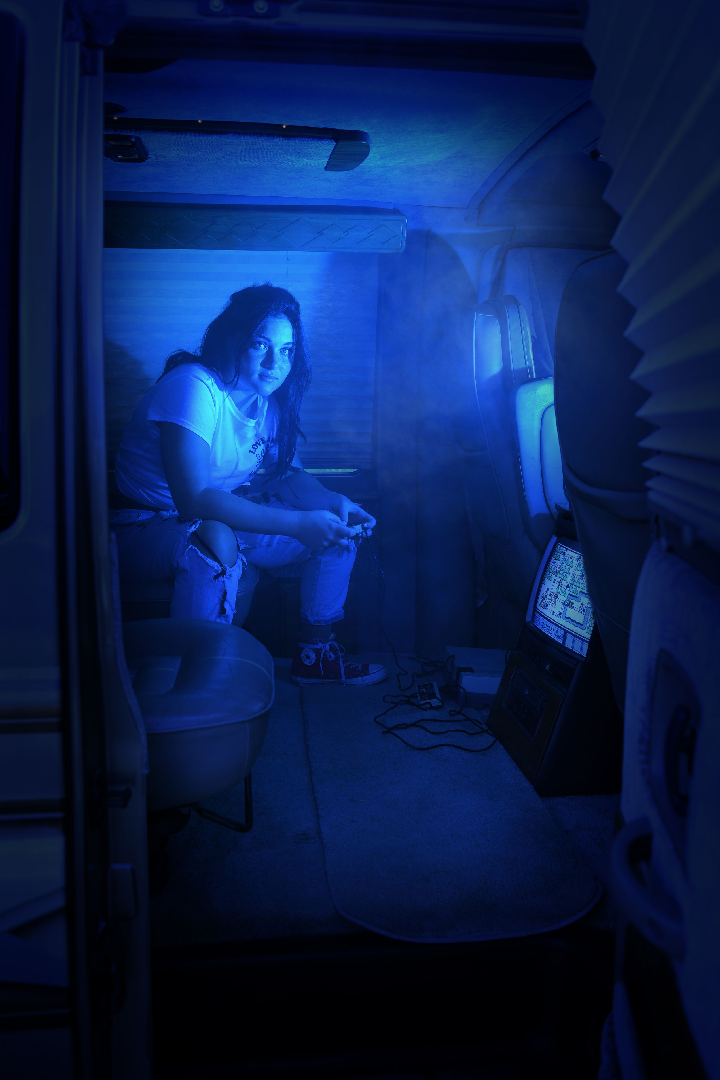 Moody blue-lit indoor portrait in confined space with dramatic lighting.