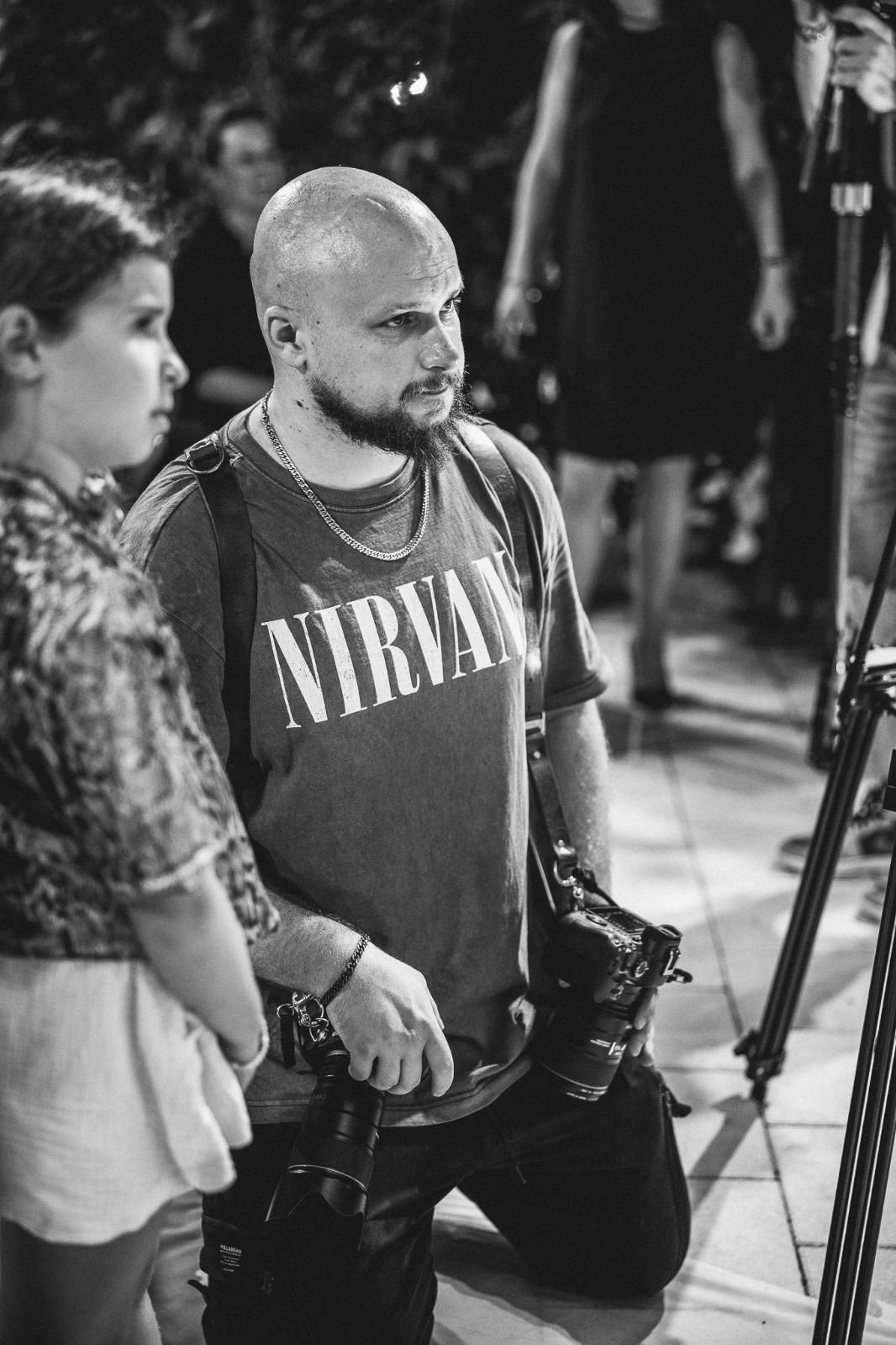Black and white photo of photographer wearing Nirvana shirt with professional cameras.