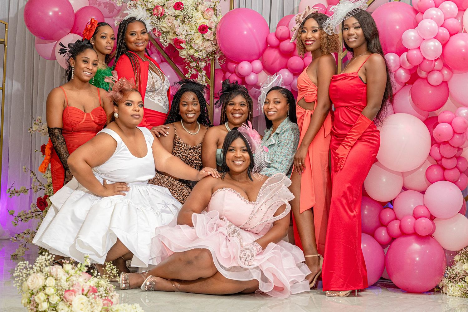Group of women posing together at a pink balloon and floral party backdrop.