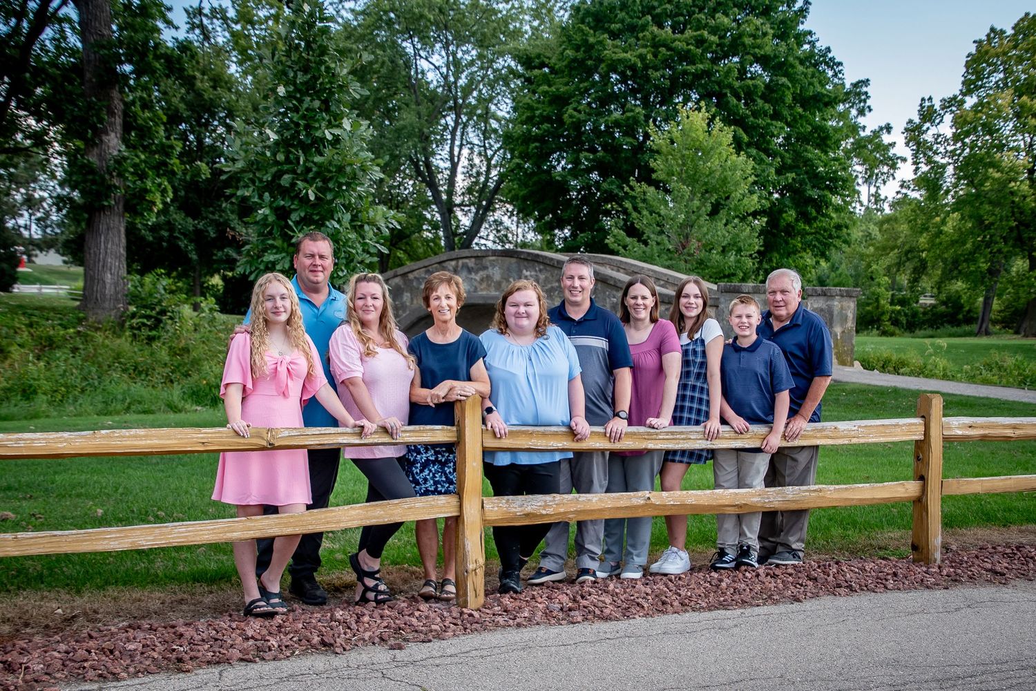 Family members lined up along wooden fence railing in scenic outdoor park setting.