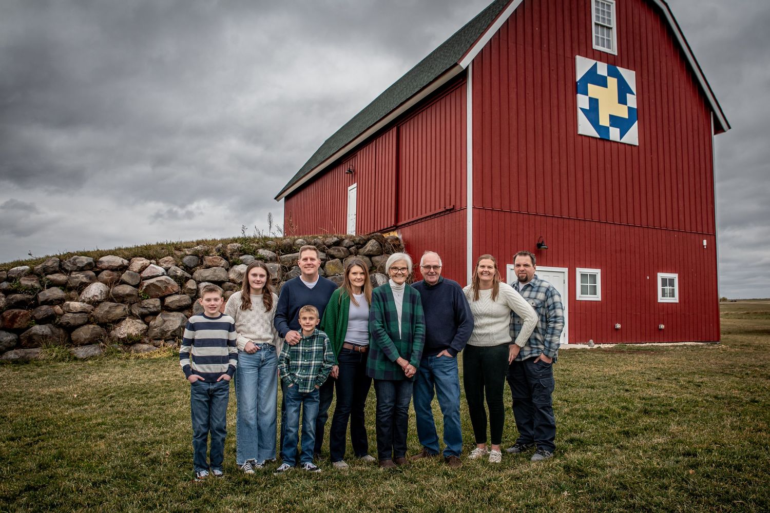 Family portrait in front of a traditional red barn featuring a blue and white quilt pattern.