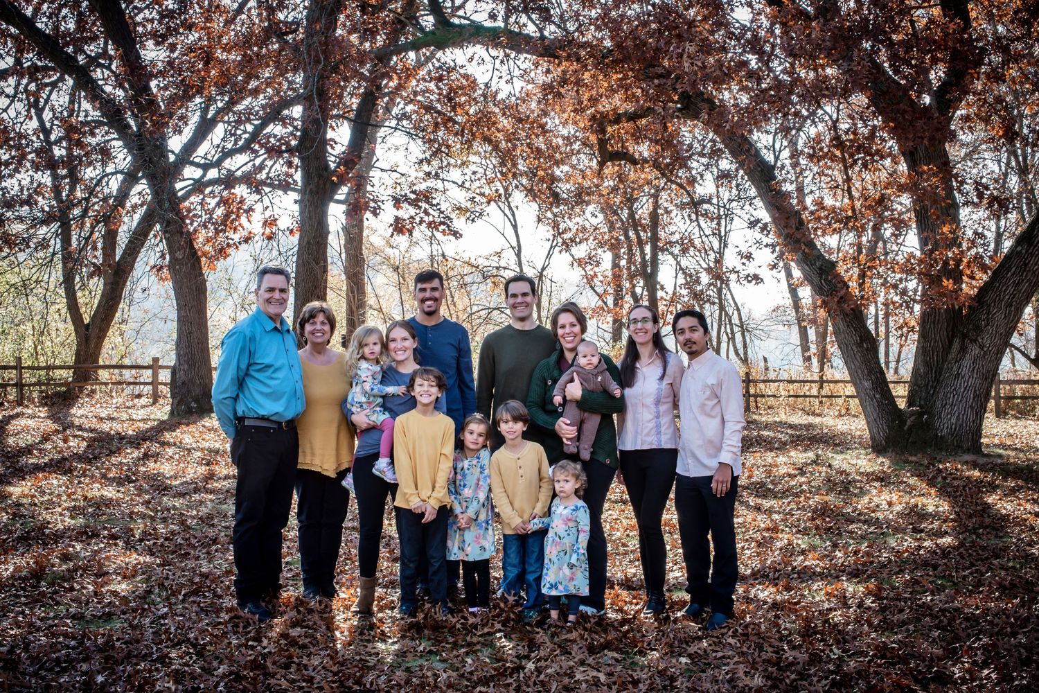 Extended family portrait taken in a wooded area with fall foliage and golden light.