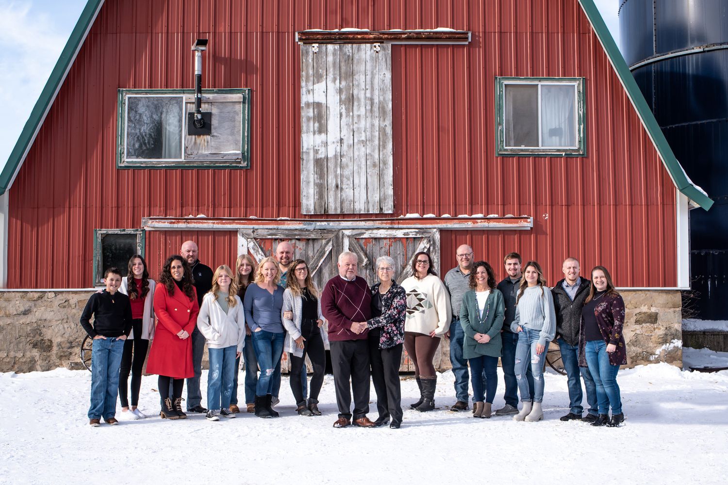 Large group gathered in front of a red barn on a snowy winter day.