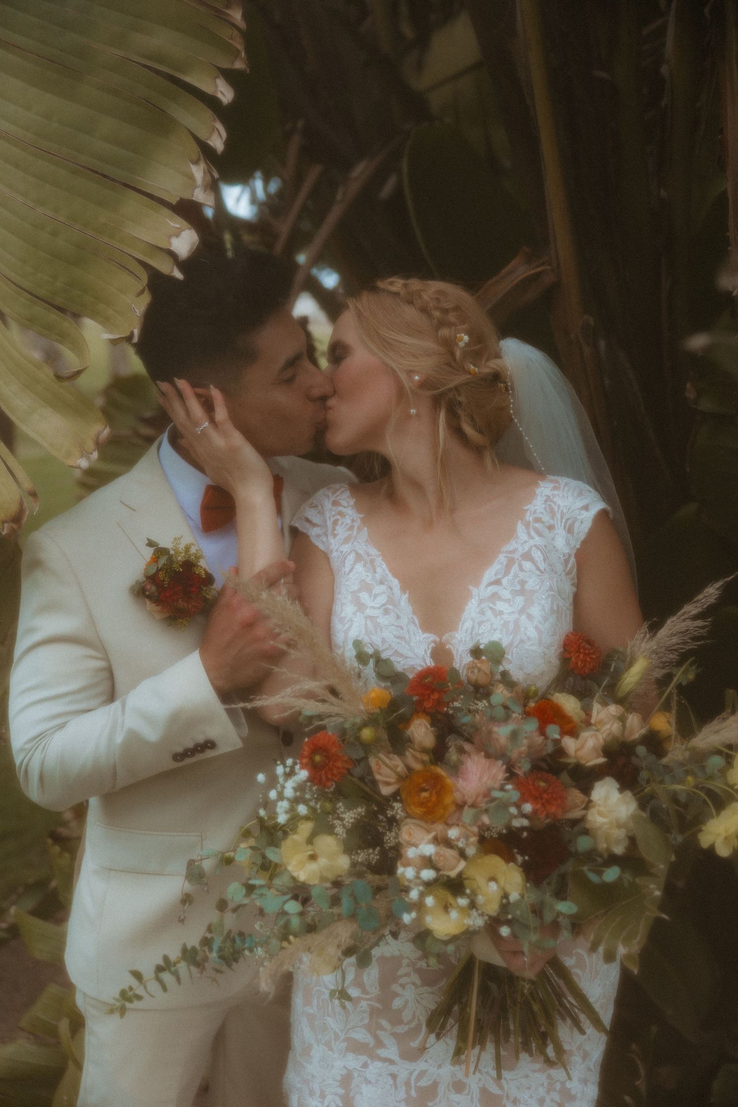 A romantic wedding moment outdoors with a beautiful bouquet of orange and white flowers under palm fronds.