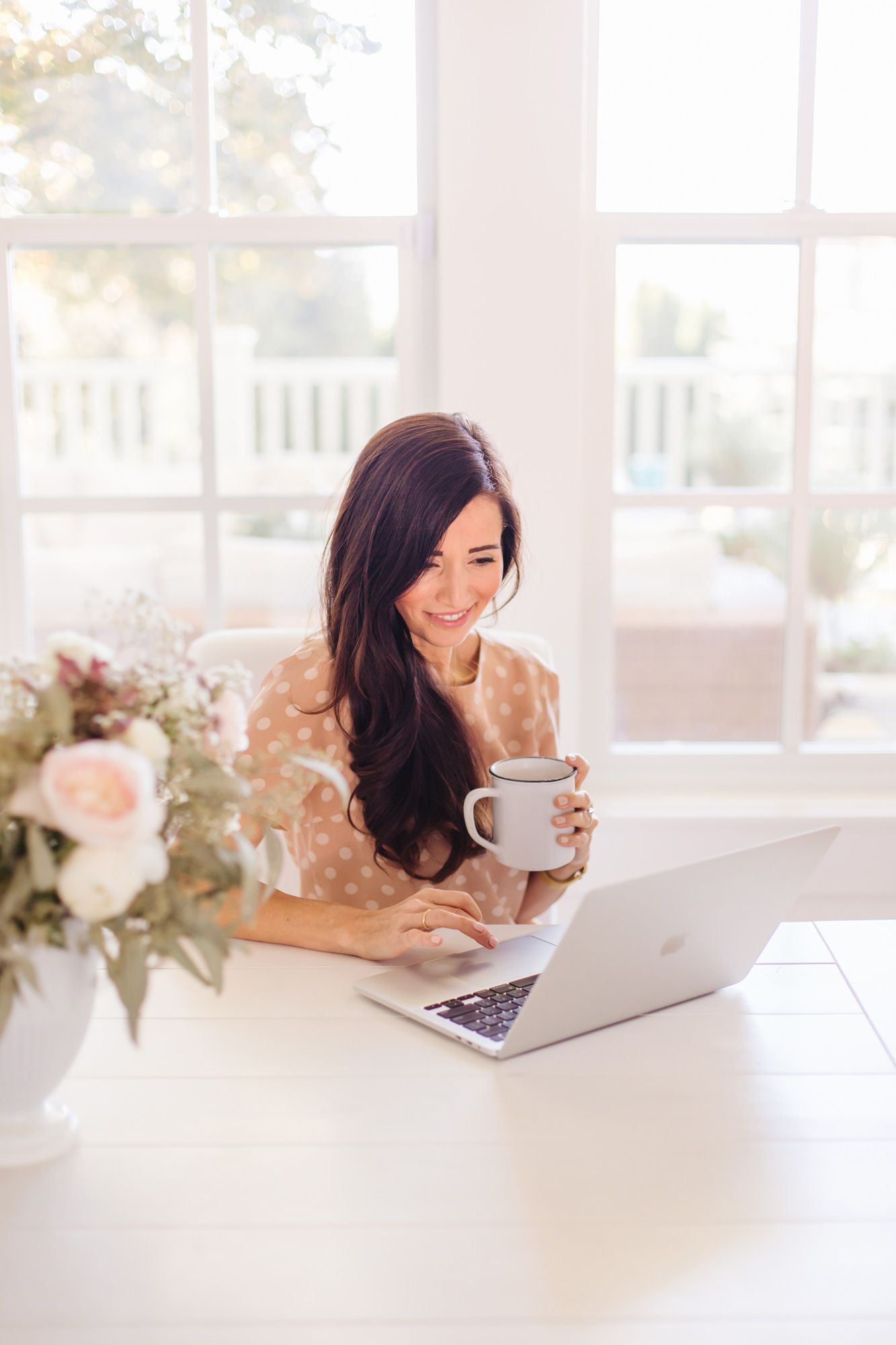 Working from home setup with laptop, coffee and floral arrangement on white desk.