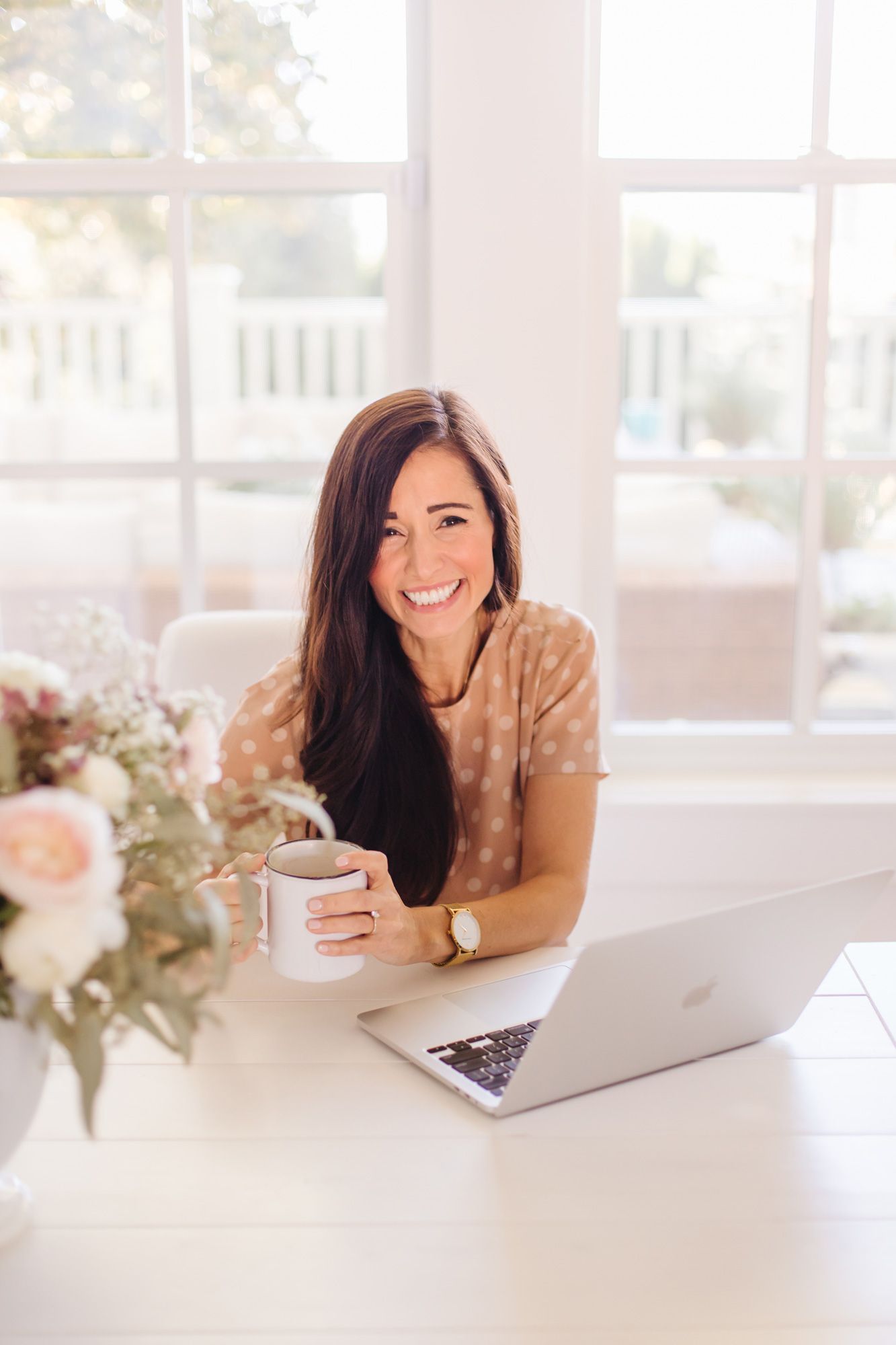 Casual home office setup with laptop and fresh flowers by sunny window.
