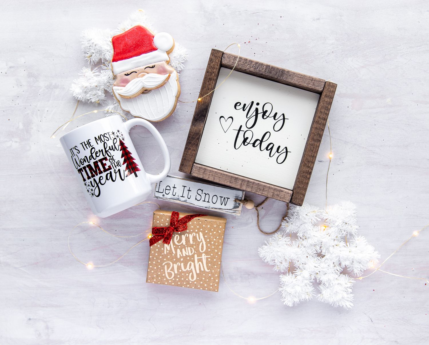 Christmas themed flat lay with Santa decorations and wooden signs on white surface.
