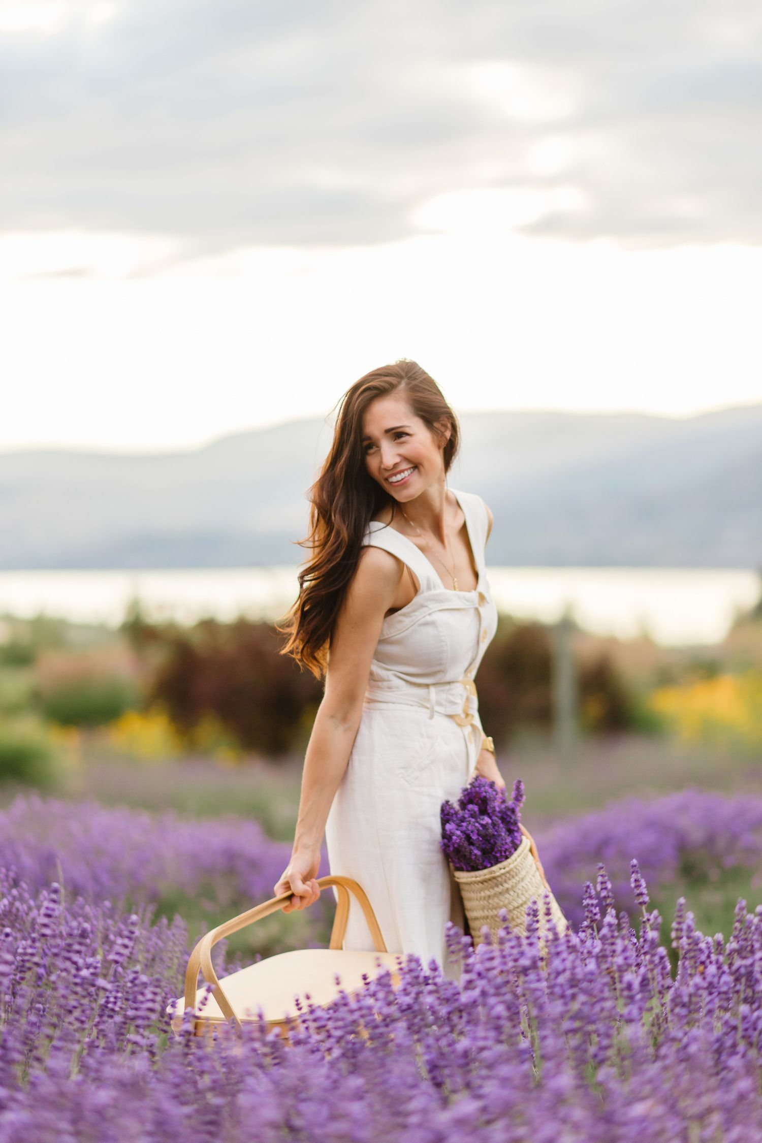 Woman in white dress walking through vibrant purple lavender field at sunset.