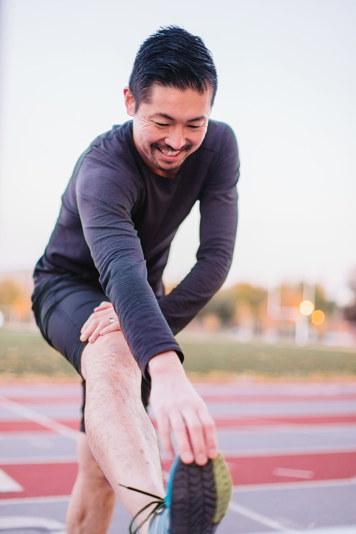 Person in grey sweater stretching and warming up on outdoor track.