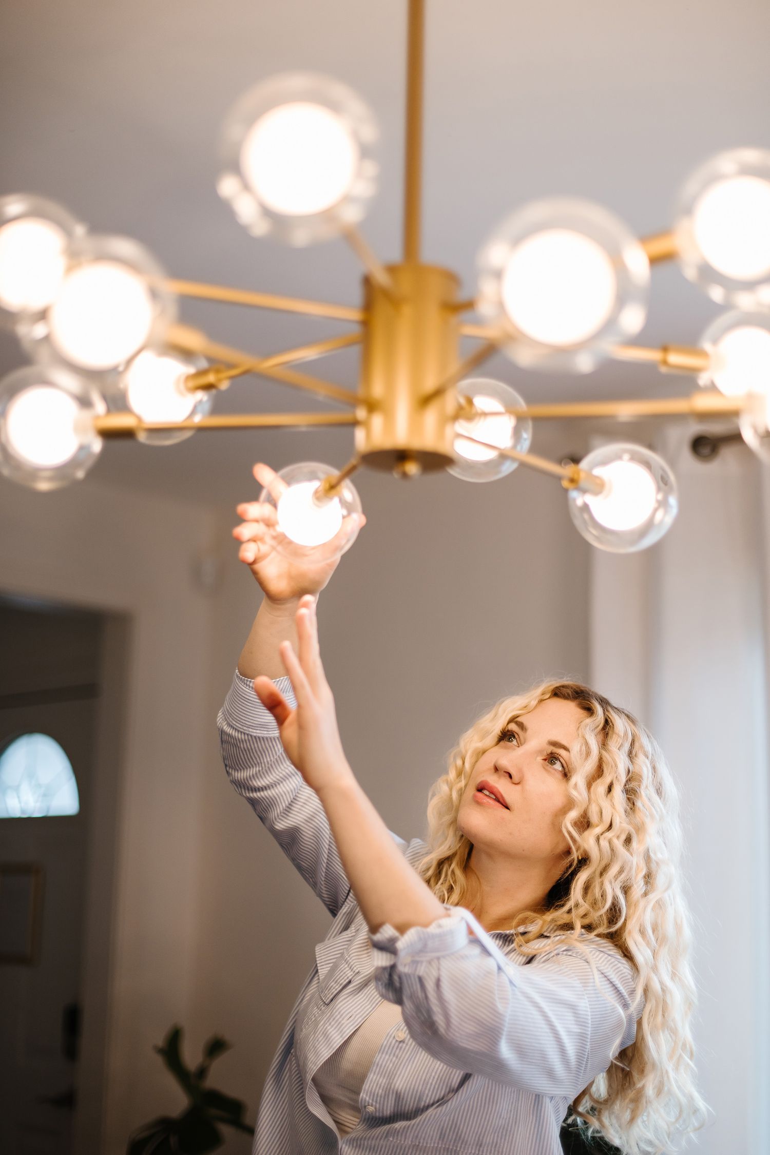 Person adjusting modern ceiling light fixture with glowing glass orbs.