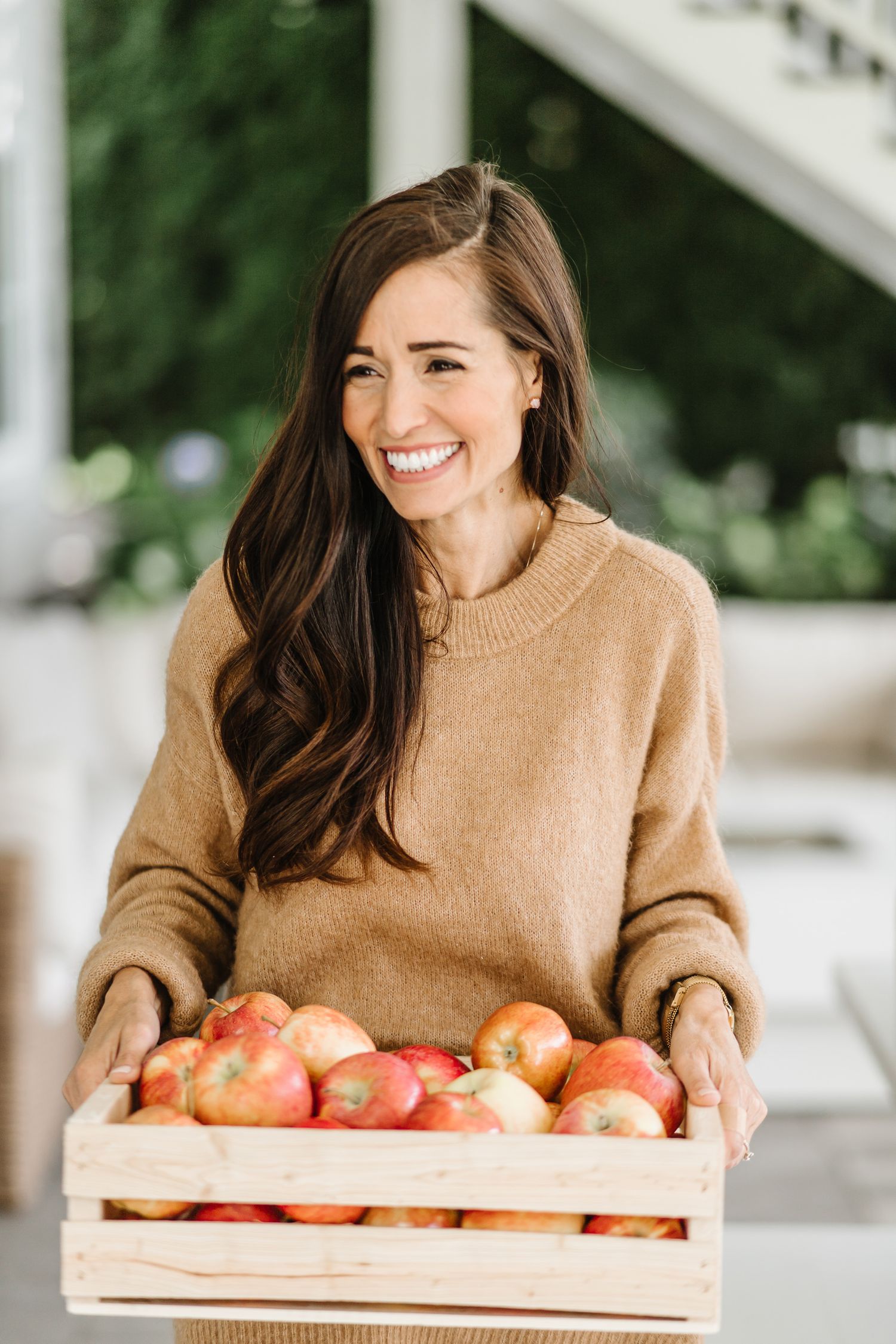 Wooden crate filled with fresh red apples being held in a cozy autumn setting.