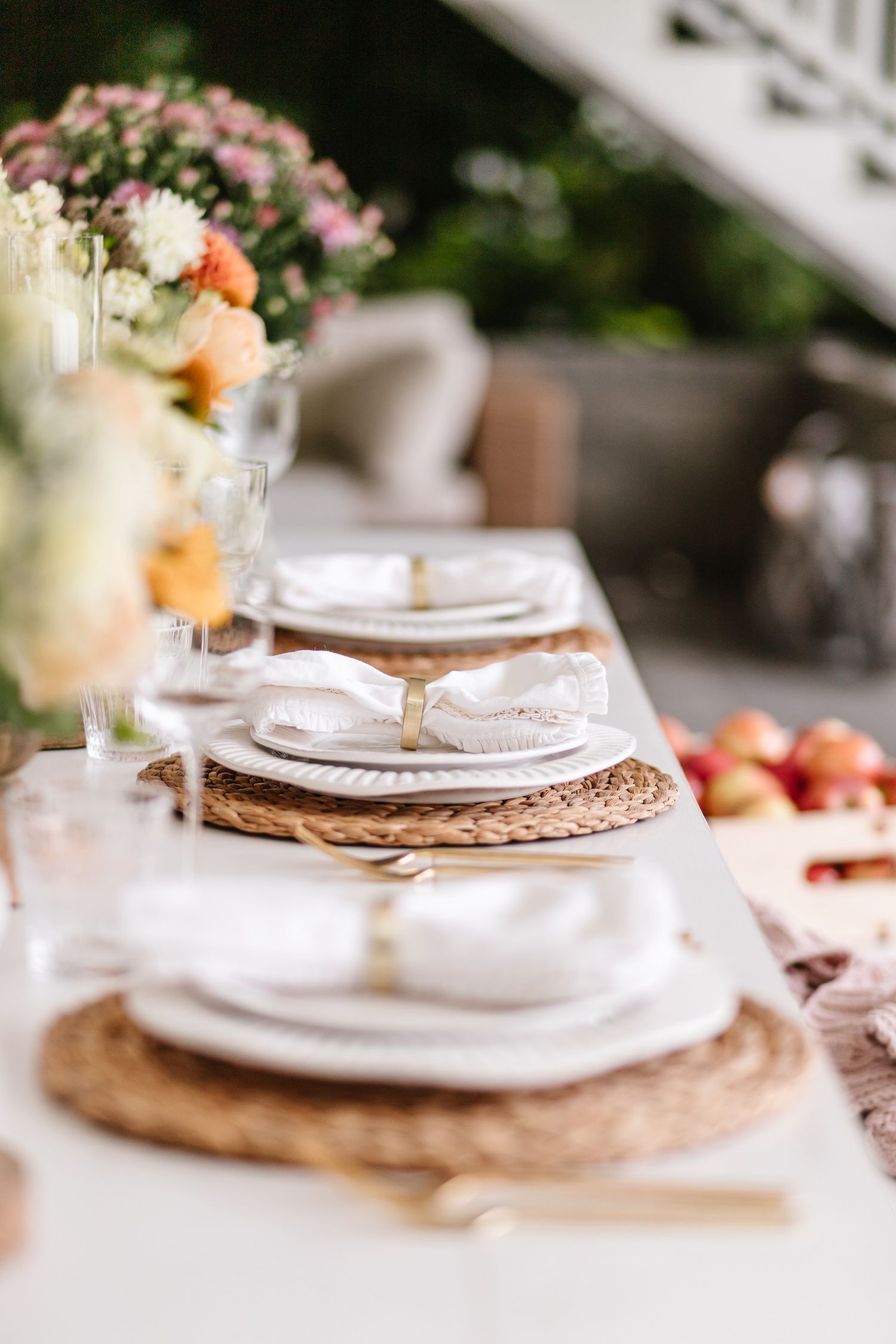 Elegant table setting with white plates, woven placemats, and pink floral arrangements.