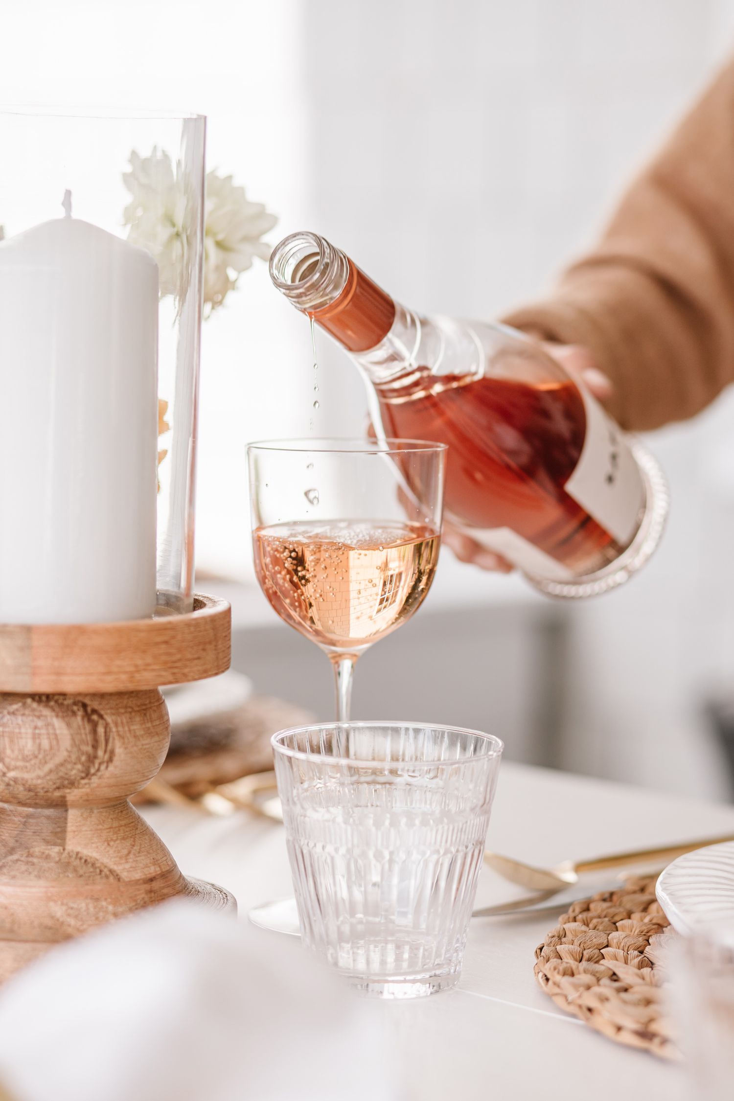 Pouring rose wine into vintage-style glass cups on a wooden surface.