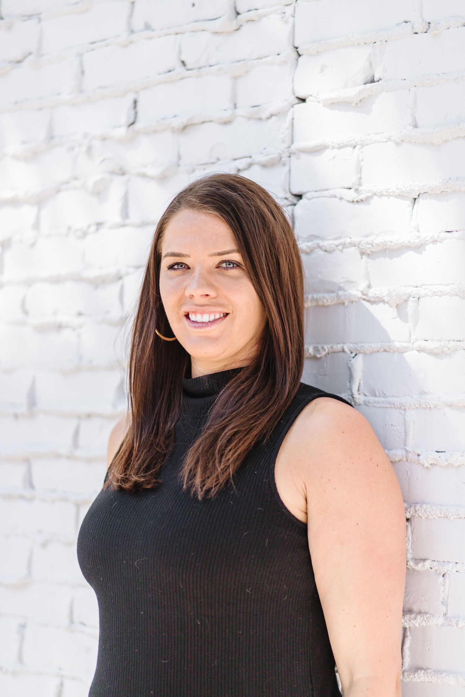 Portrait shots against a white brick wall wearing a black sleeveless top.