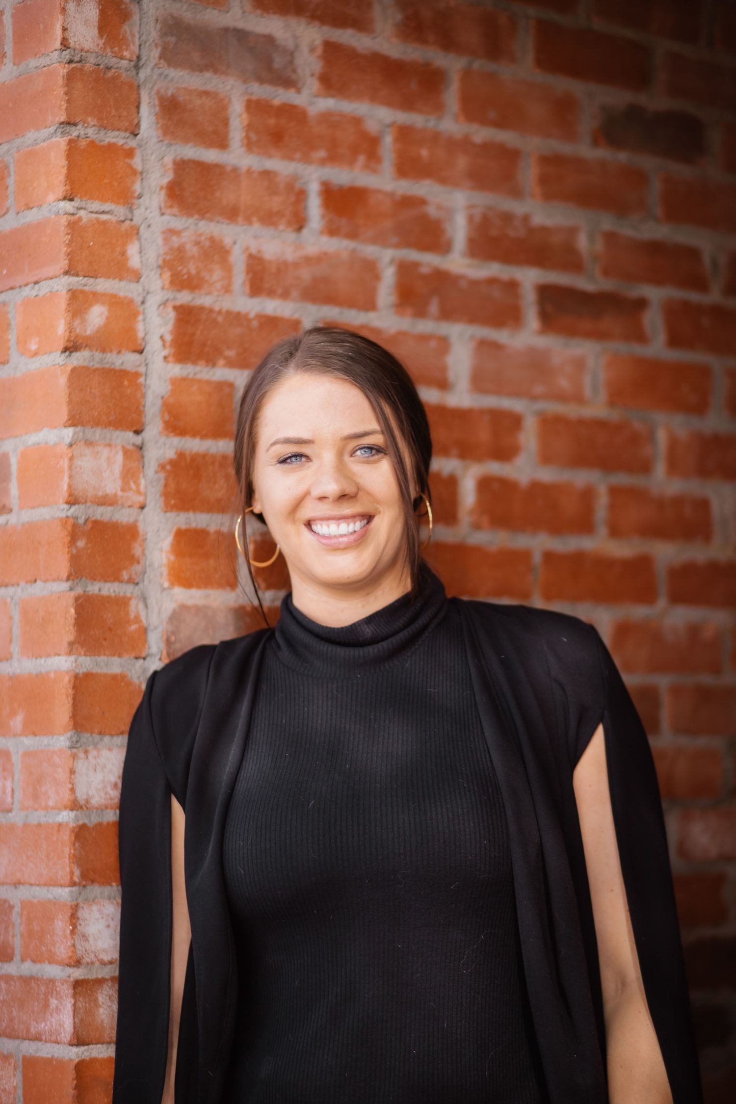 Professional headshots against a red brick wall wearing a black turtleneck.
